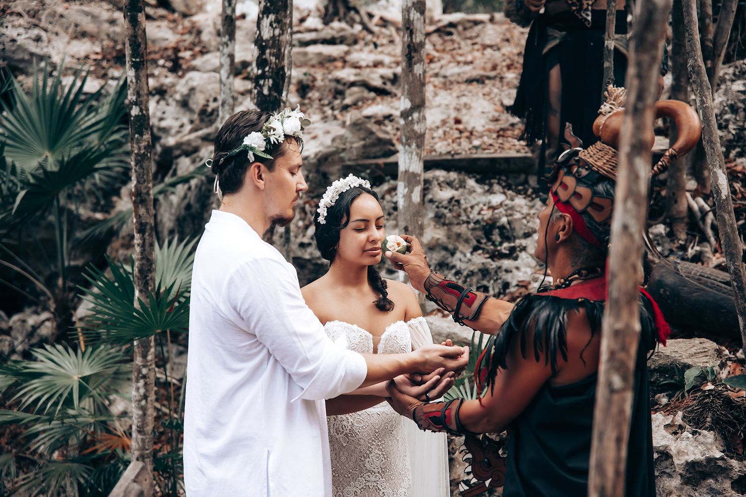 A couple participates in an intimate outdoor wedding ceremony surrounded by stone walls and tropical foliage.