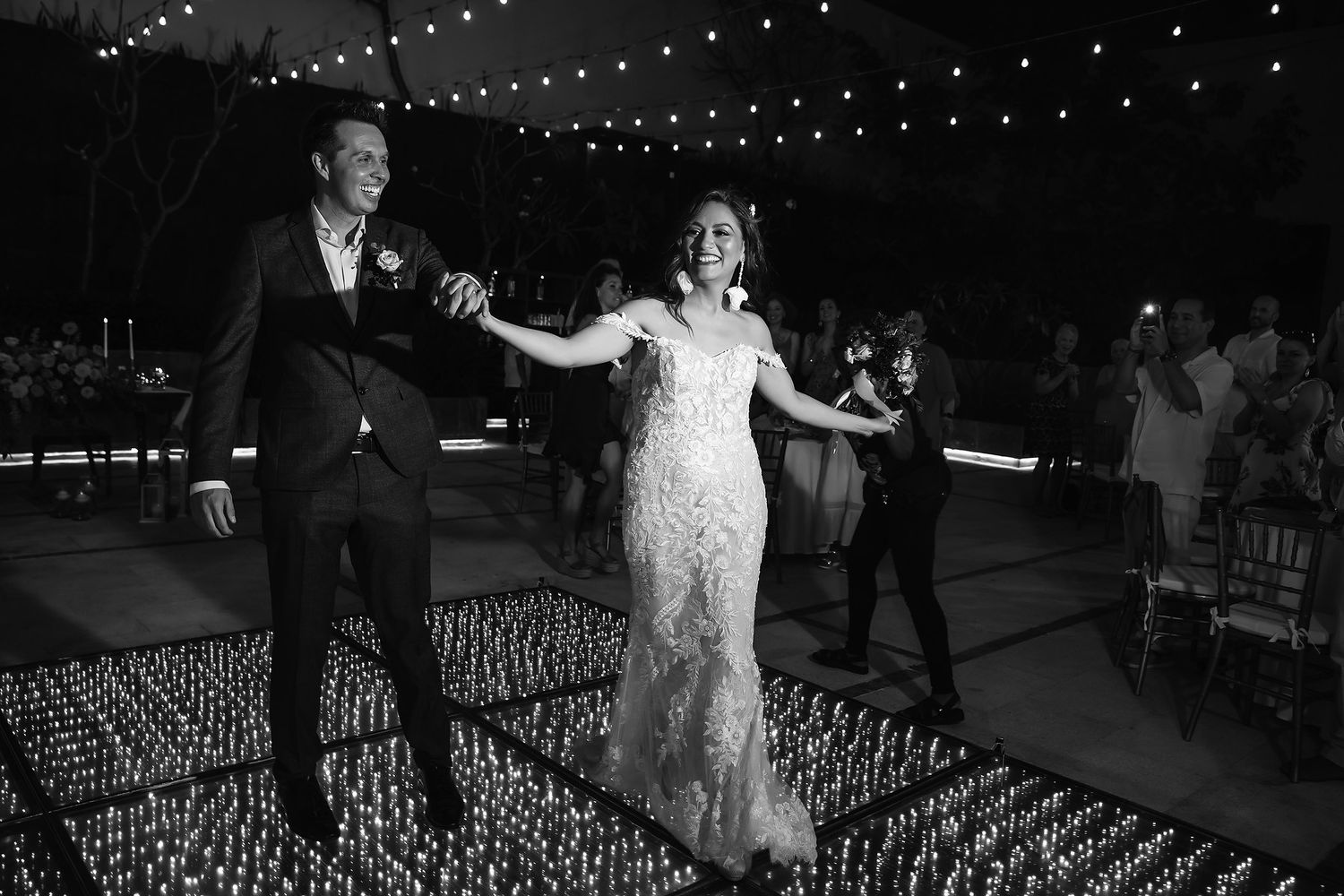 A nighttime wedding celebration with string lights illuminating an outdoor dance floor and seating area.