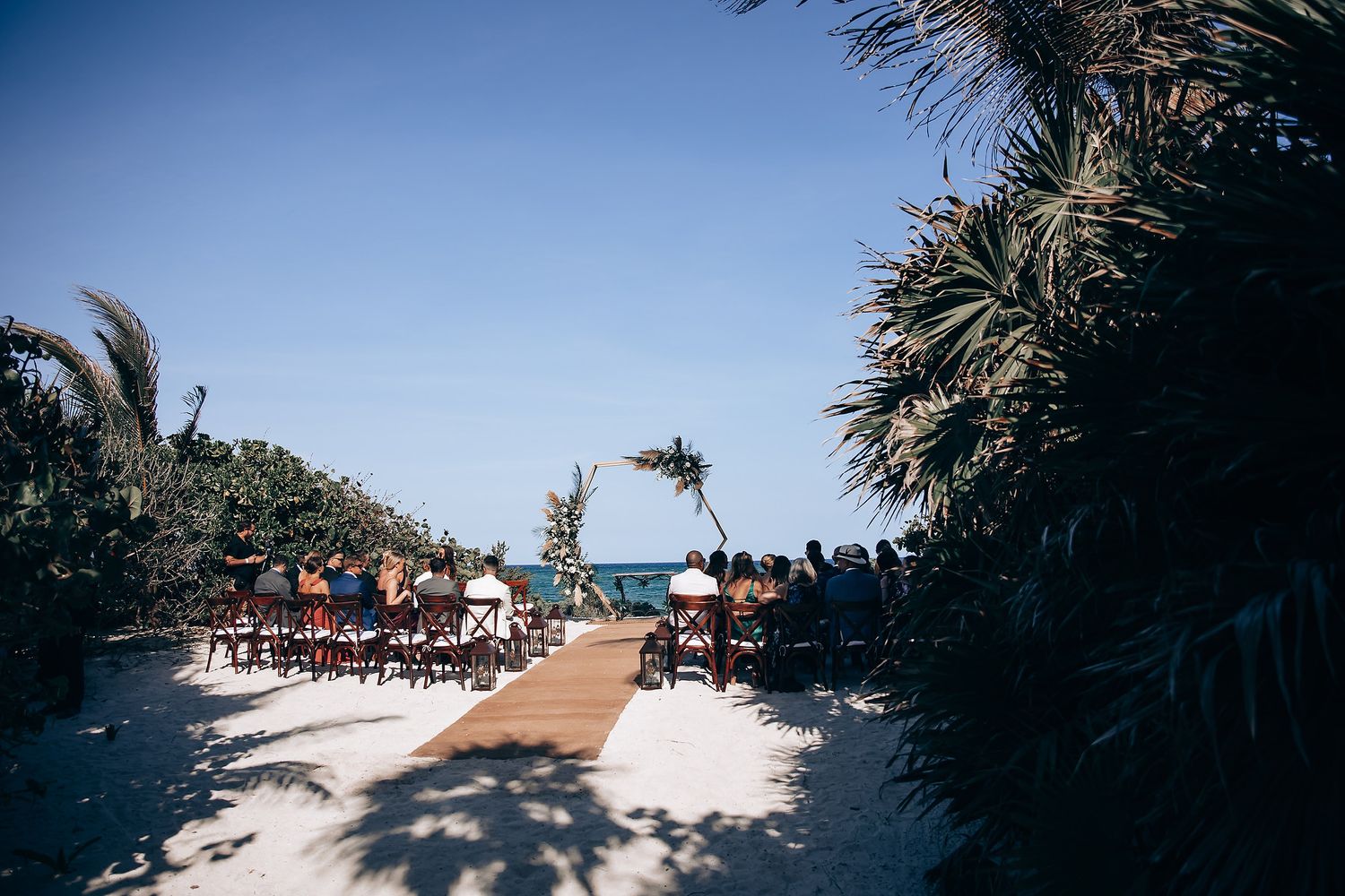 Panoramic view of a beachside wedding ceremony with palm trees and ocean in the background.