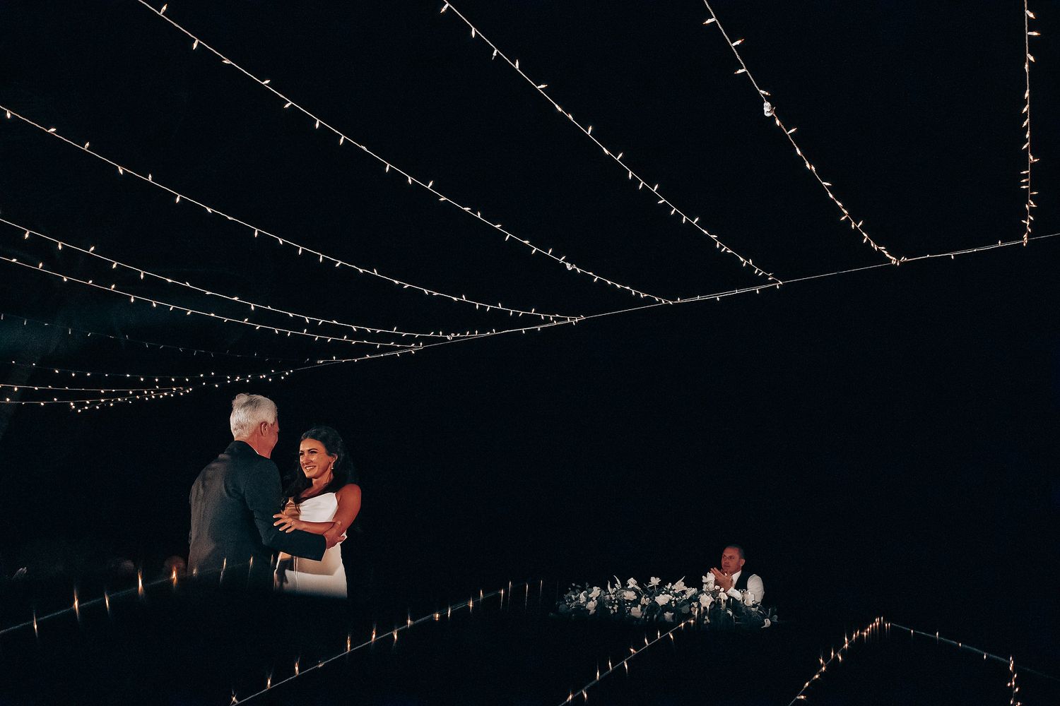 String lights create a romantic canopy over an evening wedding reception.