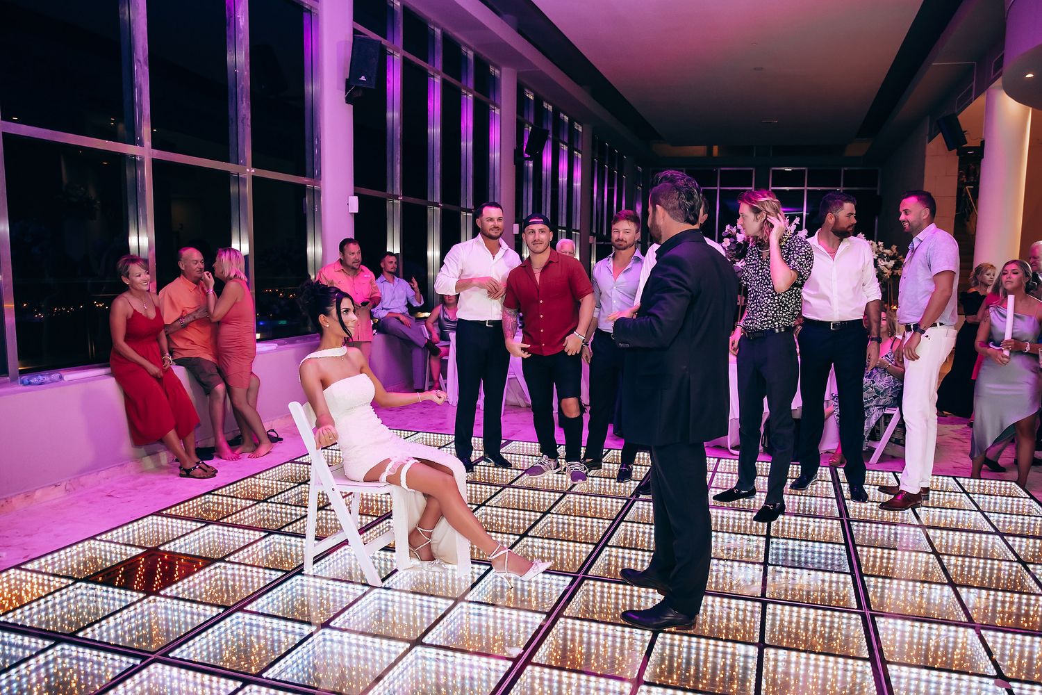 Wedding reception scene with illuminated dance floor and guests in formal attire.