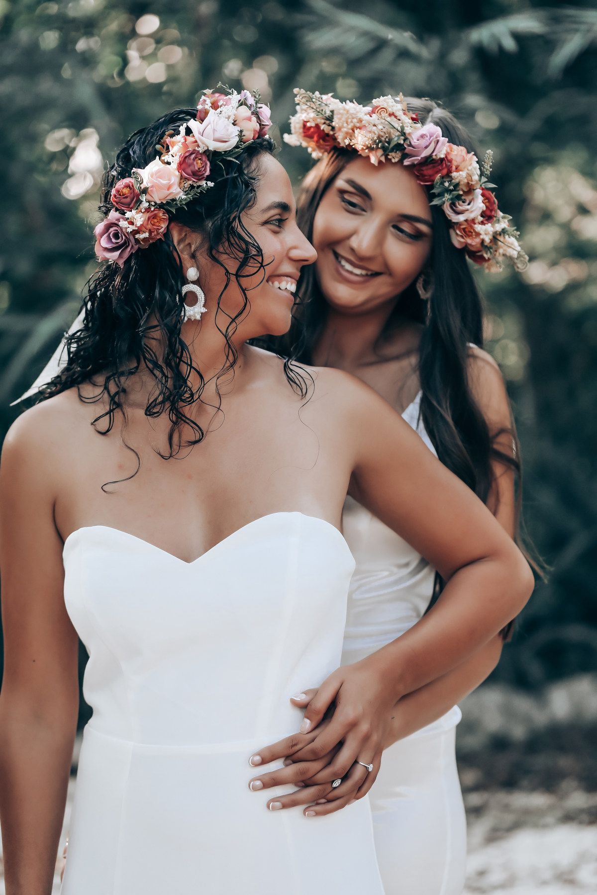 Close-up shot of two people wearing floral crowns and white dresses sharing a tender moment.