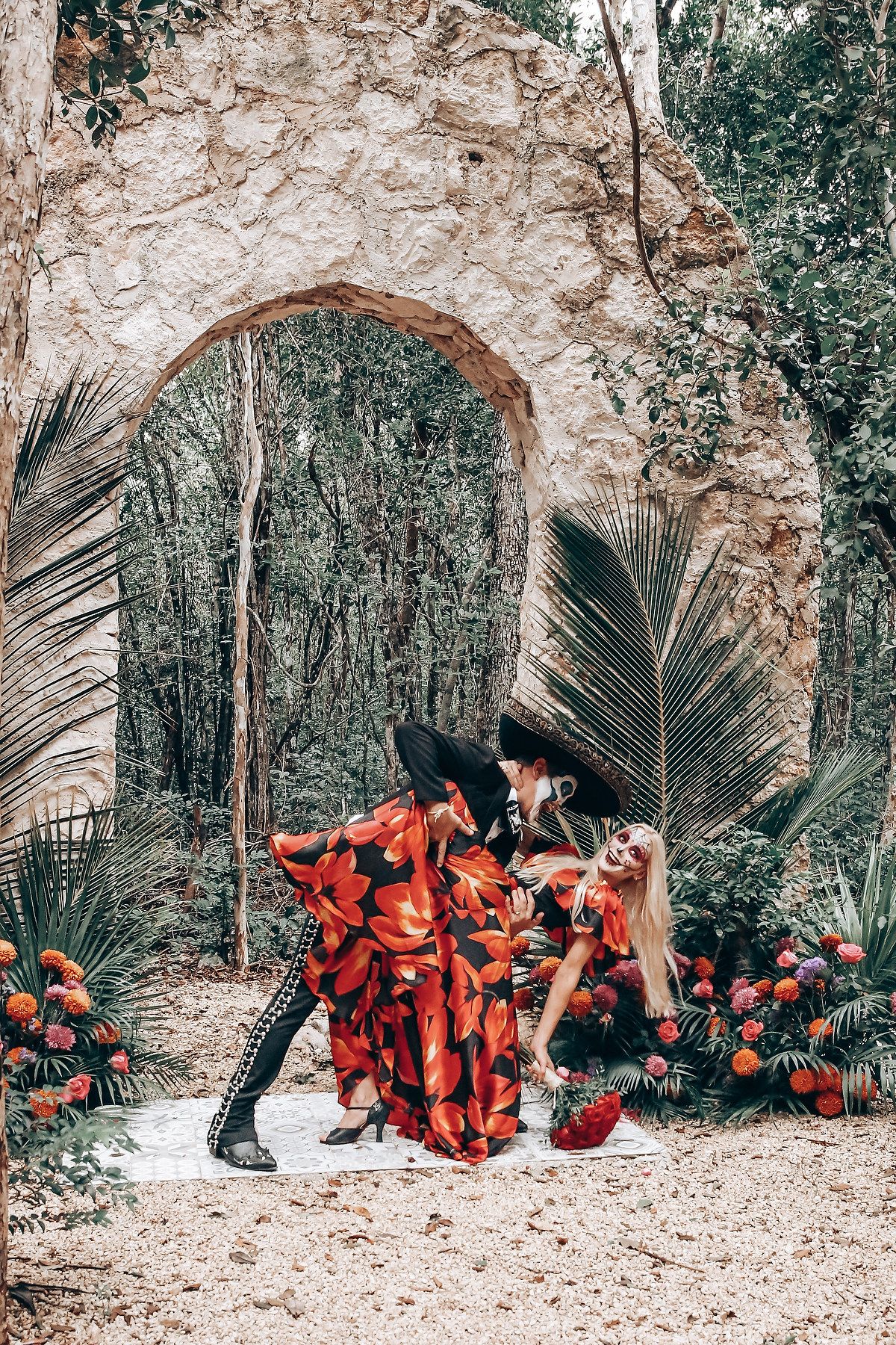 Red dress fabric flows dramatically against stone archways and tropical foliage.