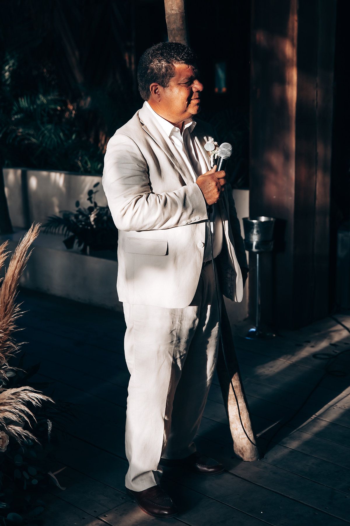 Person in a white suit giving a speech or toast in a dimly lit venue.
