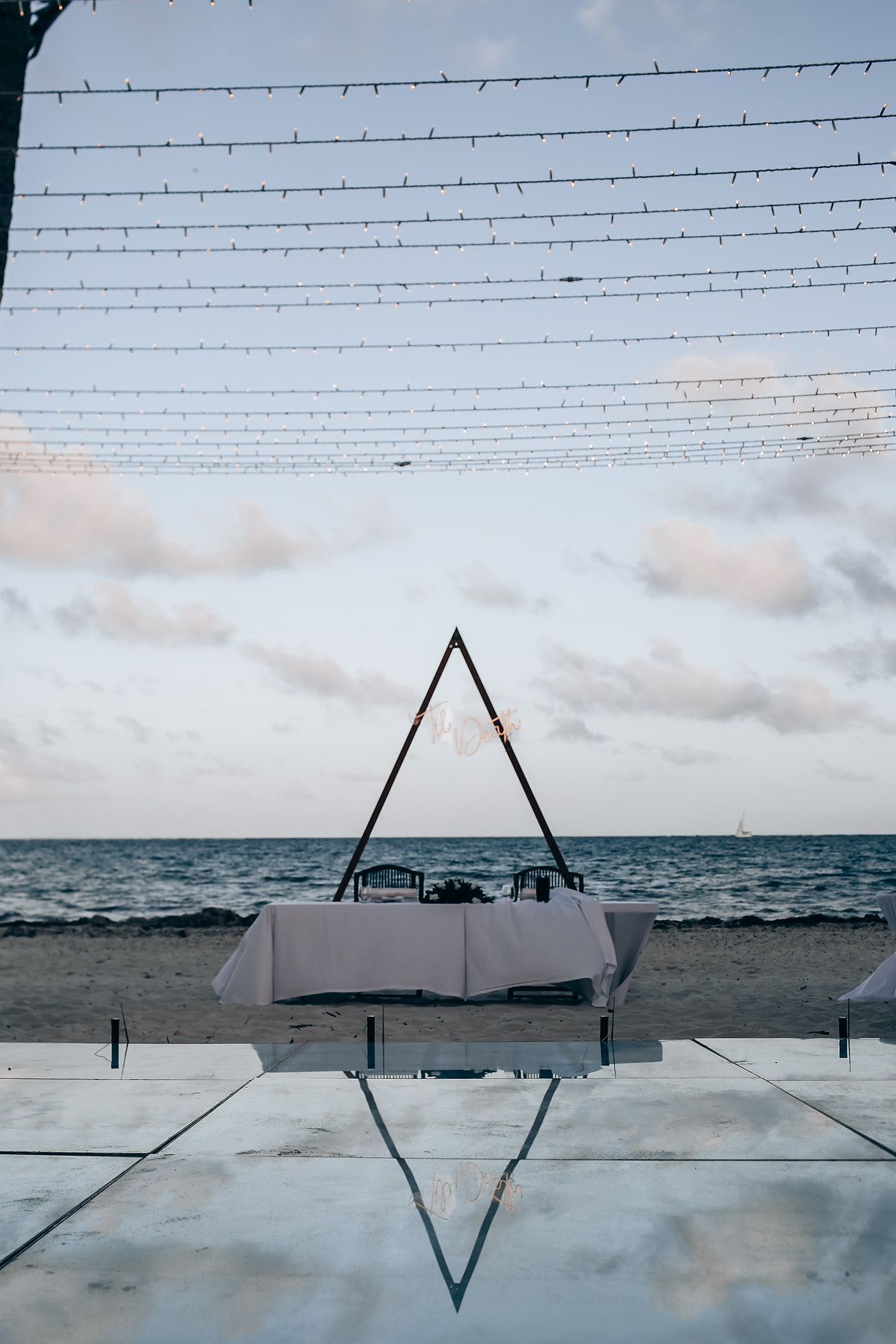String lights create geometric patterns against a cloudy sky over an oceanfront wedding venue.