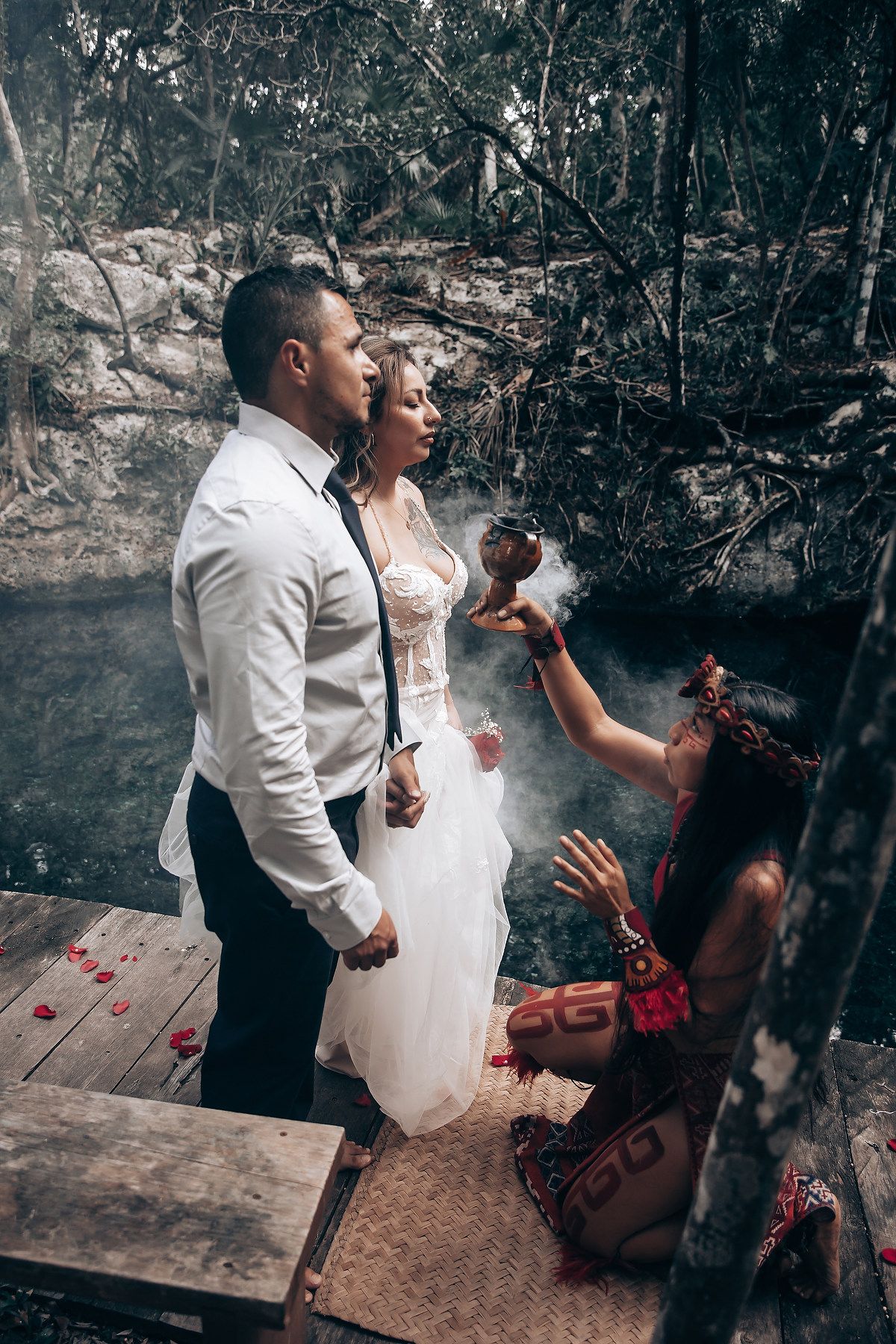 A dramatic wedding photoshoot in a dark forest setting with smoke and theatrical lighting effects.