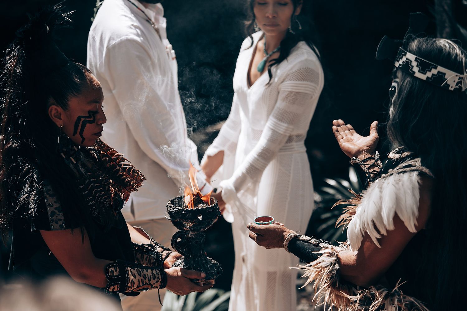 Ceremony participants in white attire gathered in a wooded area for a traditional ritual.