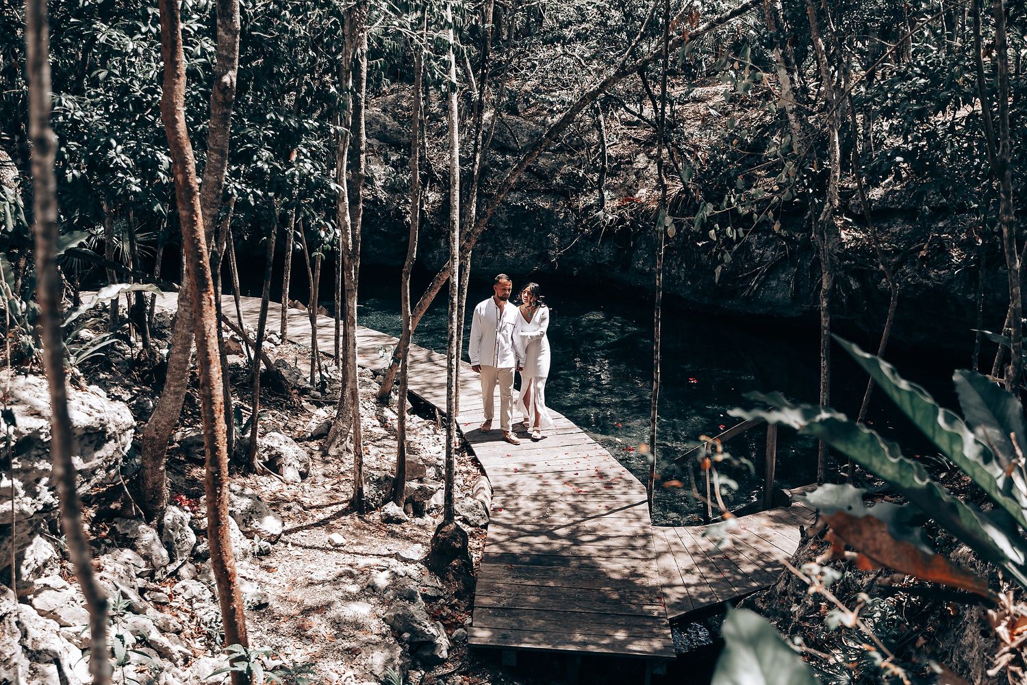 Wide view of a wooded ceremonial gathering space with attendees in white clothing.