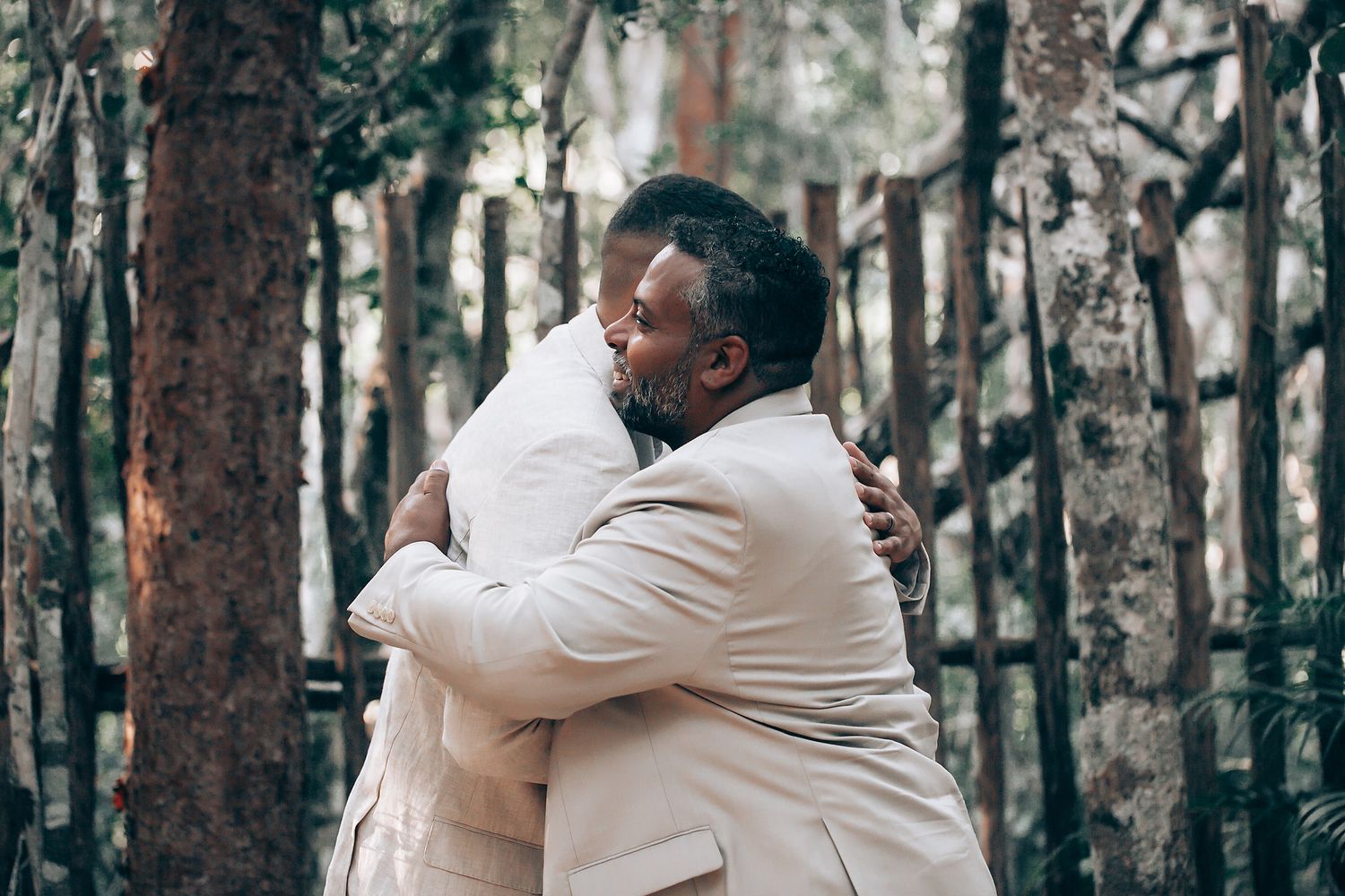 An emotional wedding moment captured in a wooded setting with natural sunlight filtering through trees.