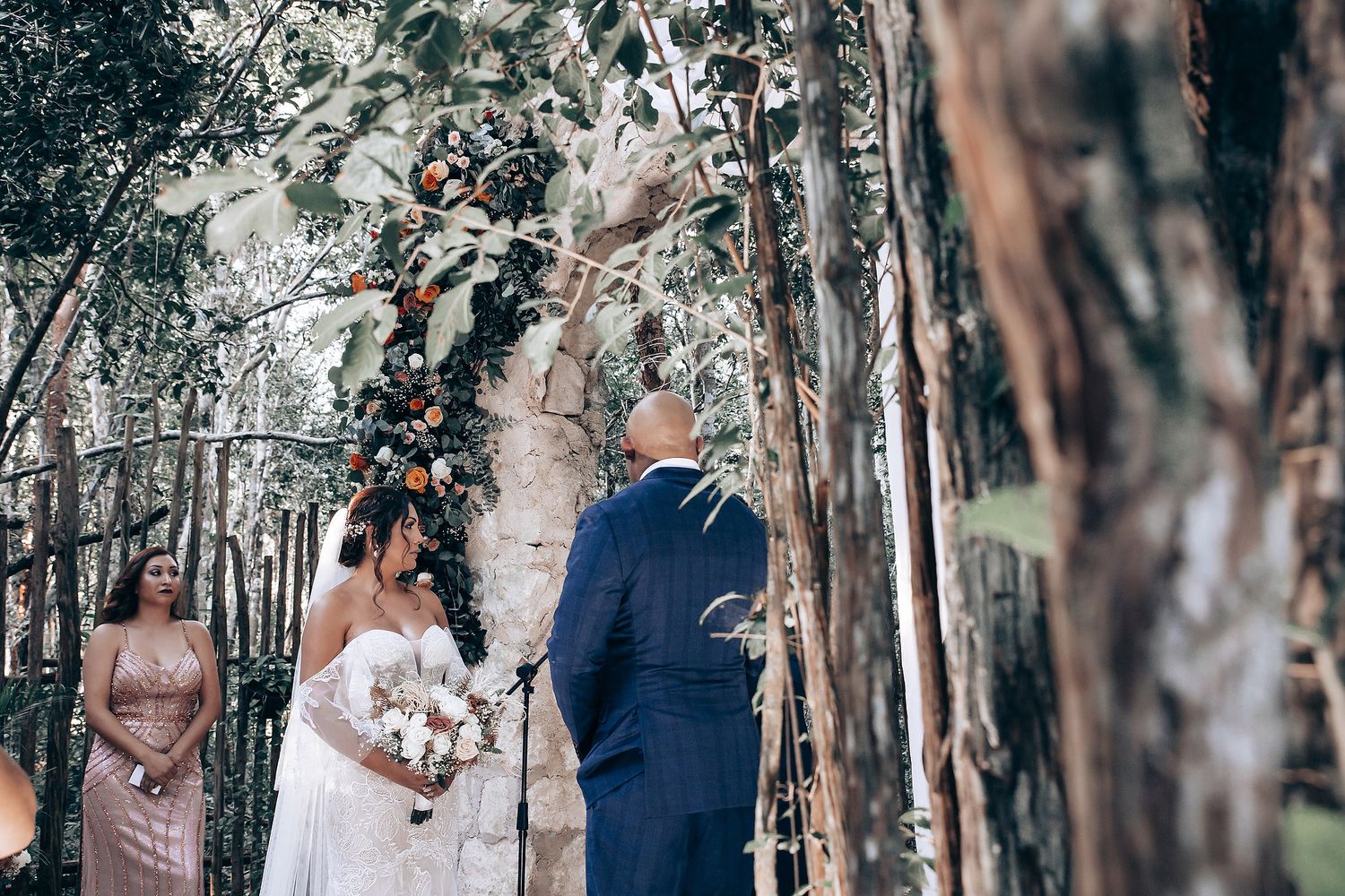 Wedding ceremony taking place in a natural forest setting with tall trees in the background.
