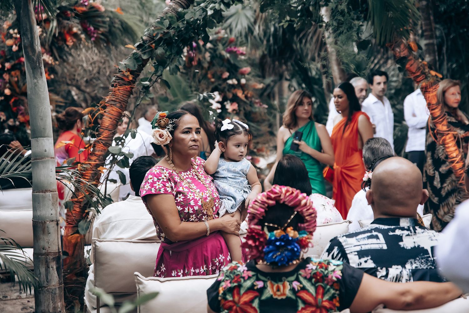 Festive outdoor celebration with people in traditional Mexican clothing enjoying themselves under palm trees.