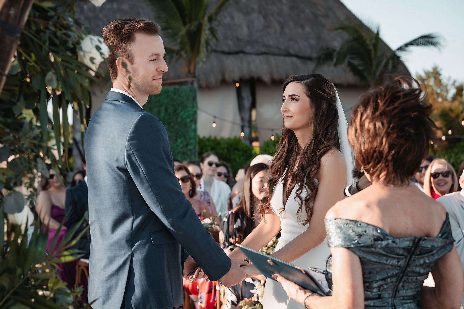 Couple exchanges vows at outdoor tropical wedding ceremony with guests seated behind them.