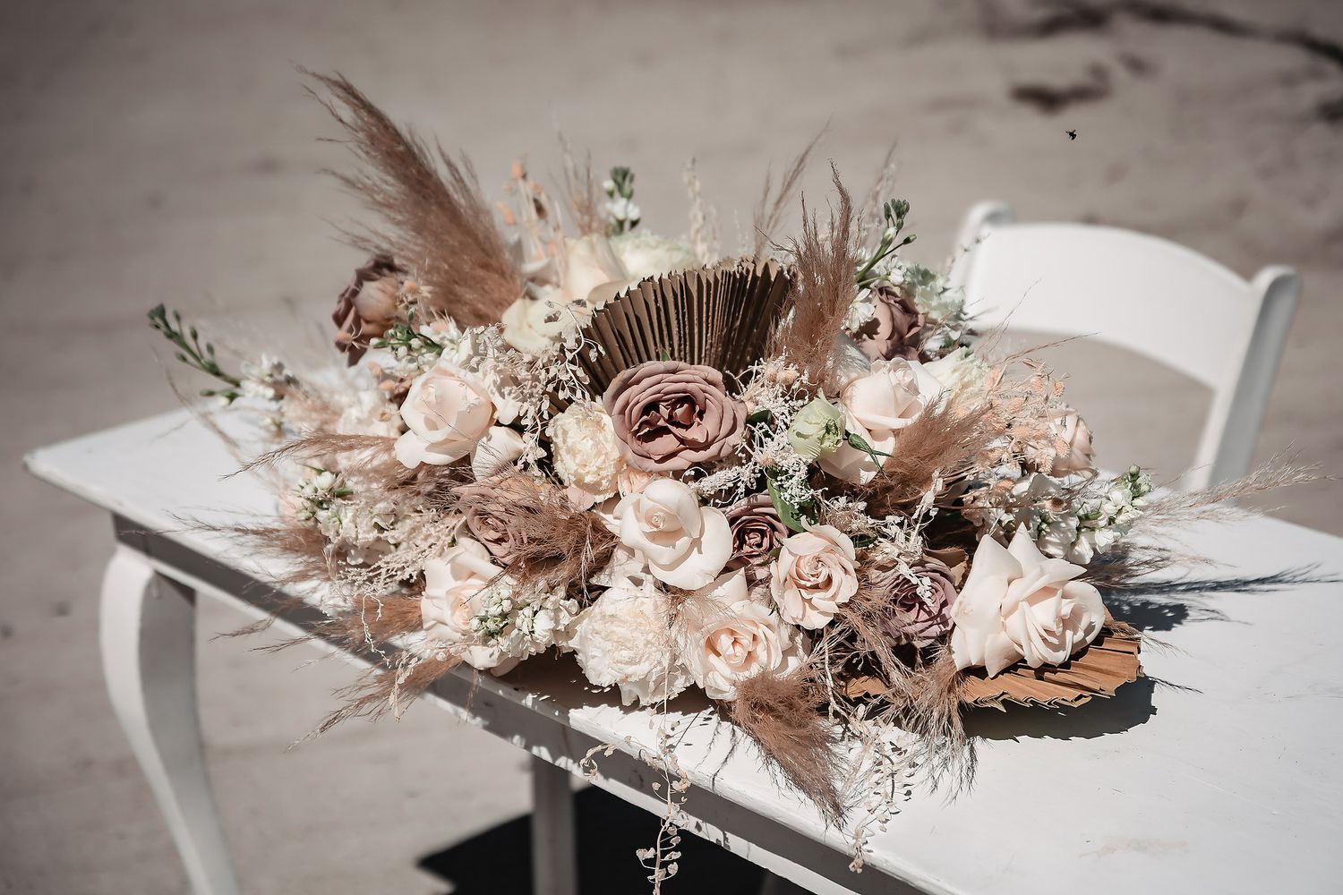 Boho wedding floral arrangement with blush roses, pampas grass, and dried flowers on a white table.