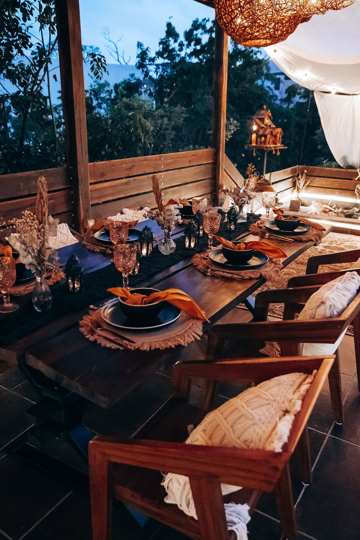 Elegant outdoor boho wedding dinner table set with black plates and candles at dusk.