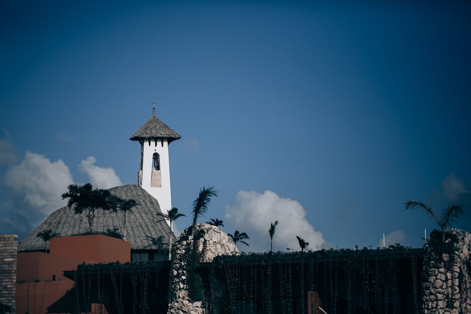 White tower with dome rises against blue sky with palm trees at a tropical resort.