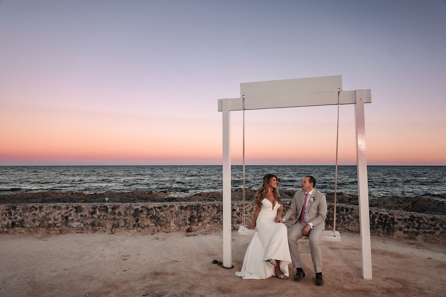 A serene beach wedding setup with white pillars against a pastel sunset sky.