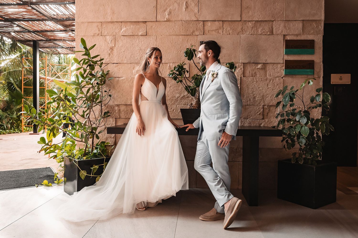 Wedding couple posing in natural light against pink stone wall and tropical plants.