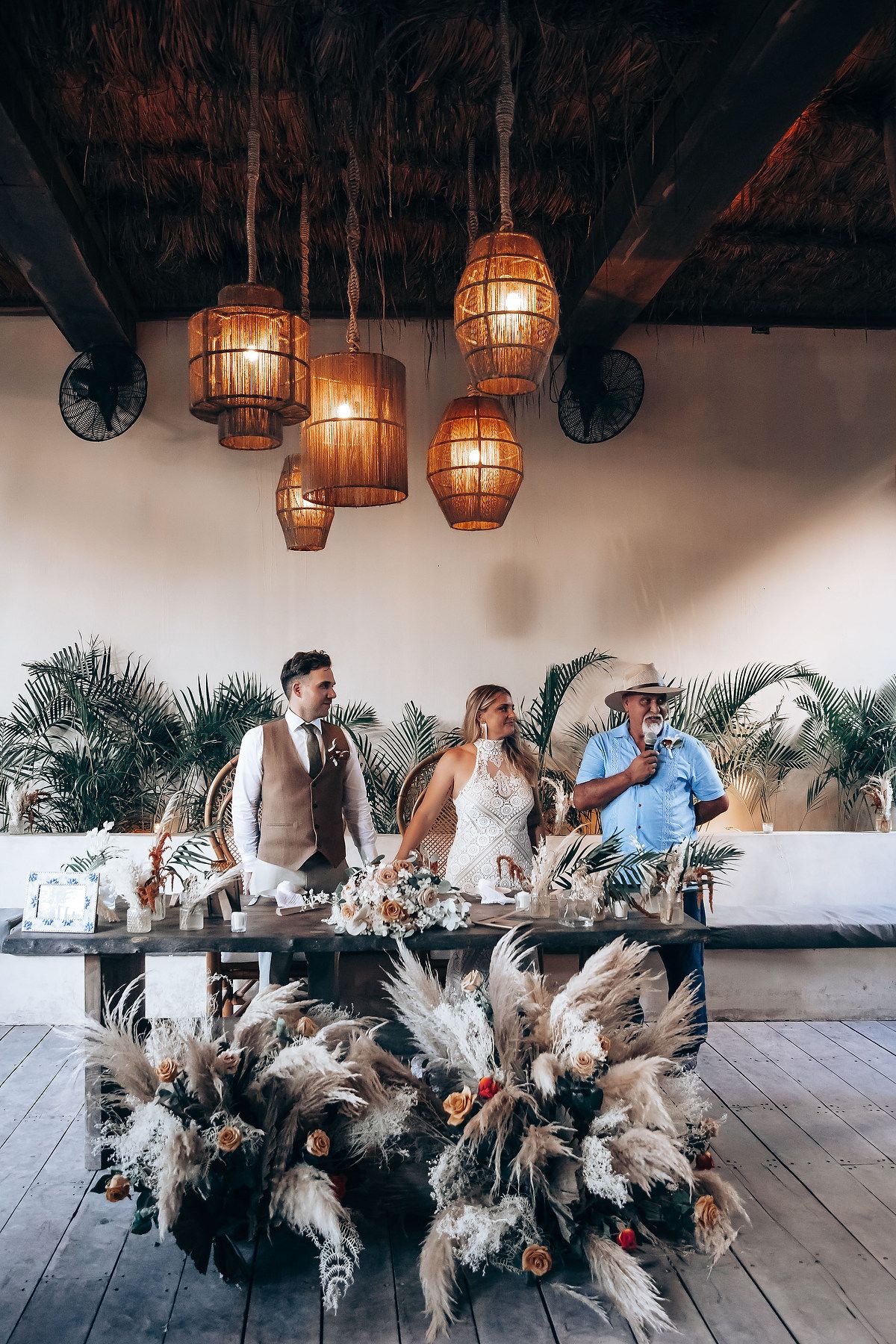 Wedding guests seated at a long table decorated with dramatic white pampas grass arrangements and hanging lanterns.