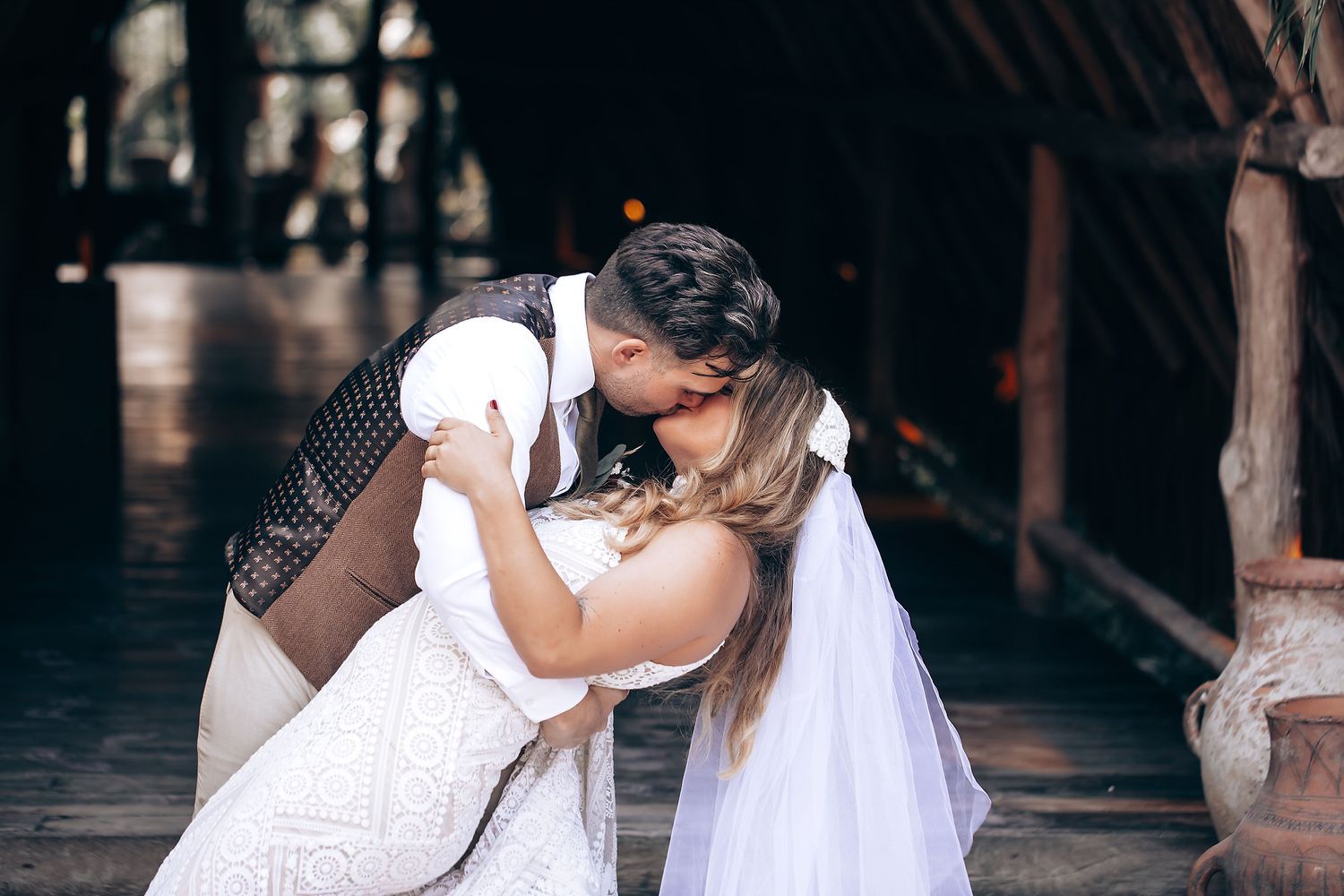 A romantic couple in wedding attire share intimate moments together in a dimly lit rustic setting.