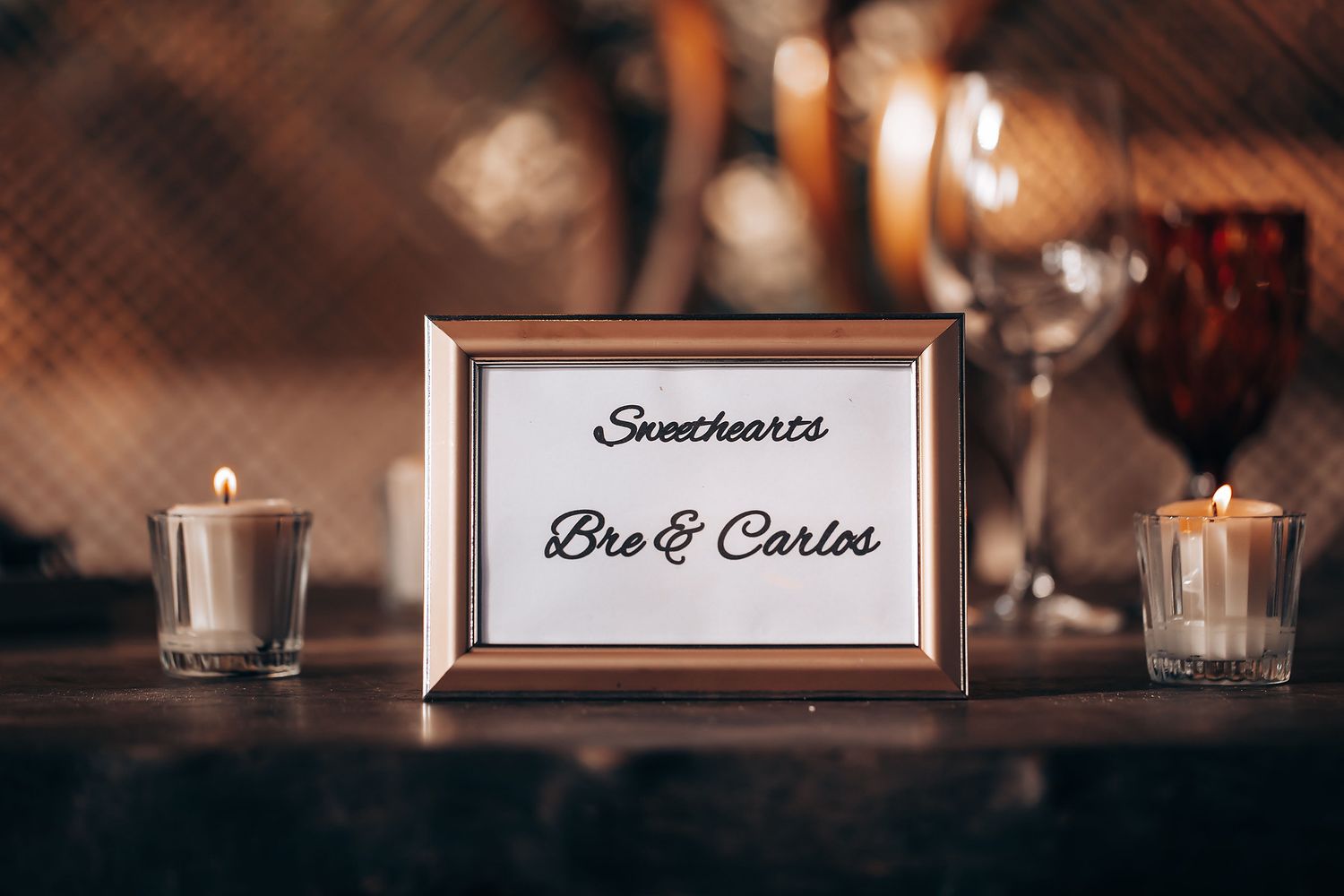 Illuminated glass candle holders and decorative signage create an elegant ambiance at a dimly lit event venue.