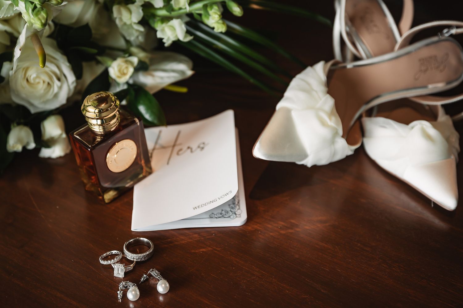 Wedding rings and floral decor arranged on a dark wooden surface at a reception.