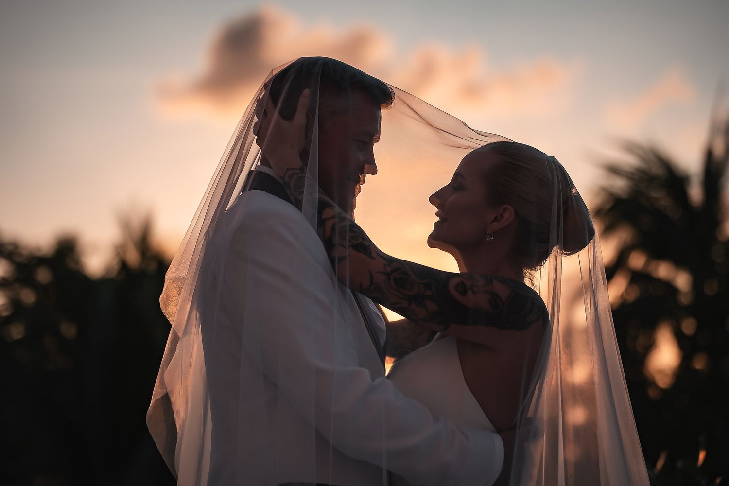 Romantic silhouettes of a couple against a sunset sky with palm trees in the background.