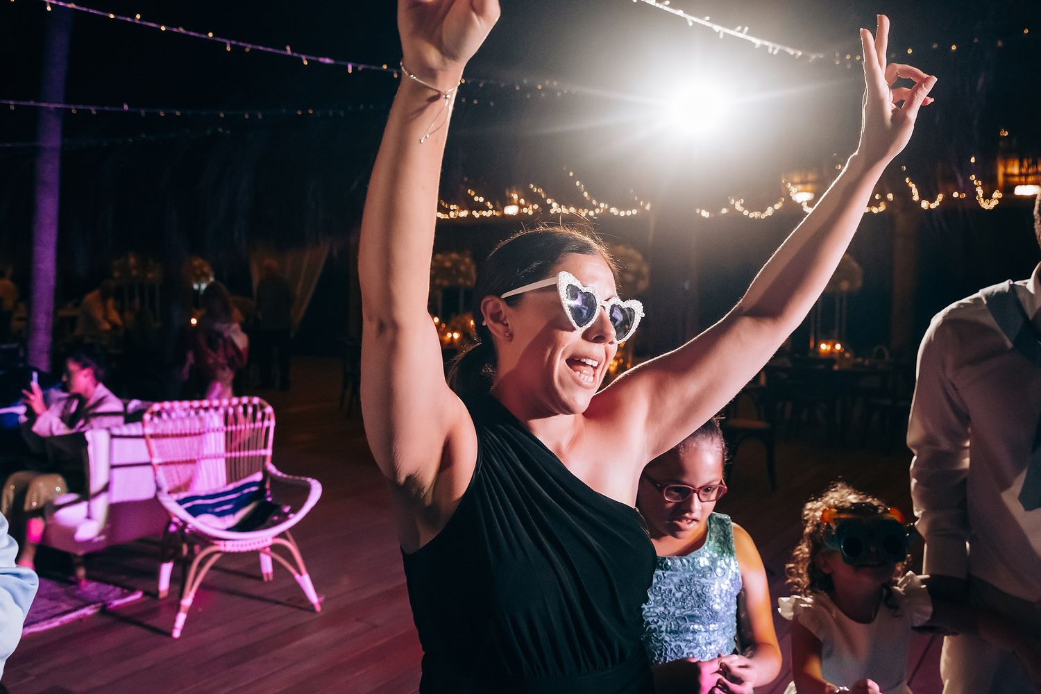Wedding reception dance floor illuminated with purple lighting and string lights overhead.