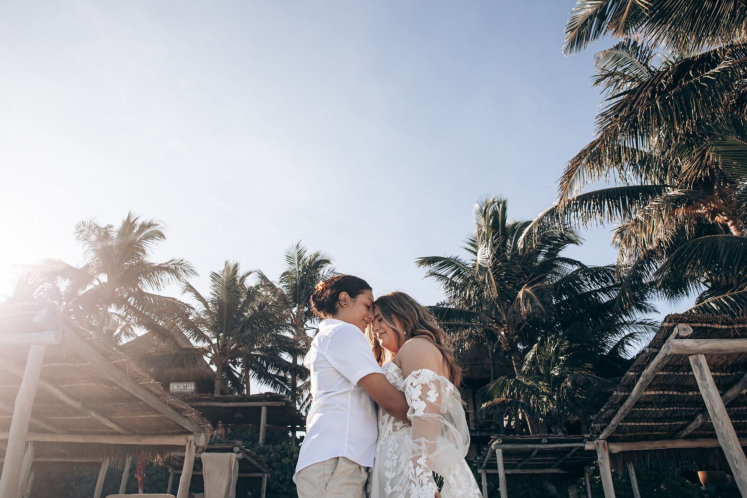 Couple embracing on a tropical beach with palm trees and golden sunlight filtering through.