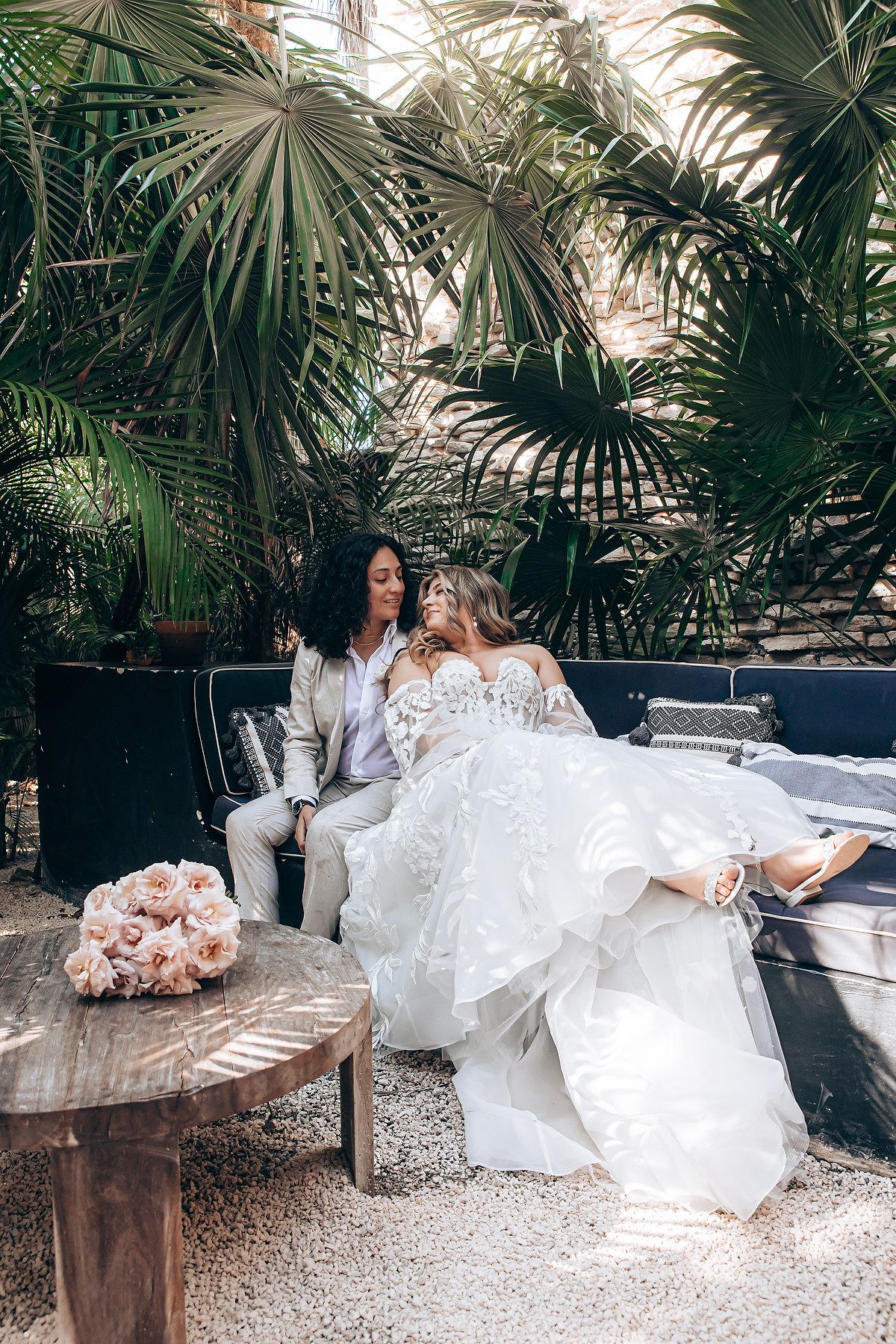 A wedding photoshoot in a tropical garden setting with palm trees and rustic furniture.