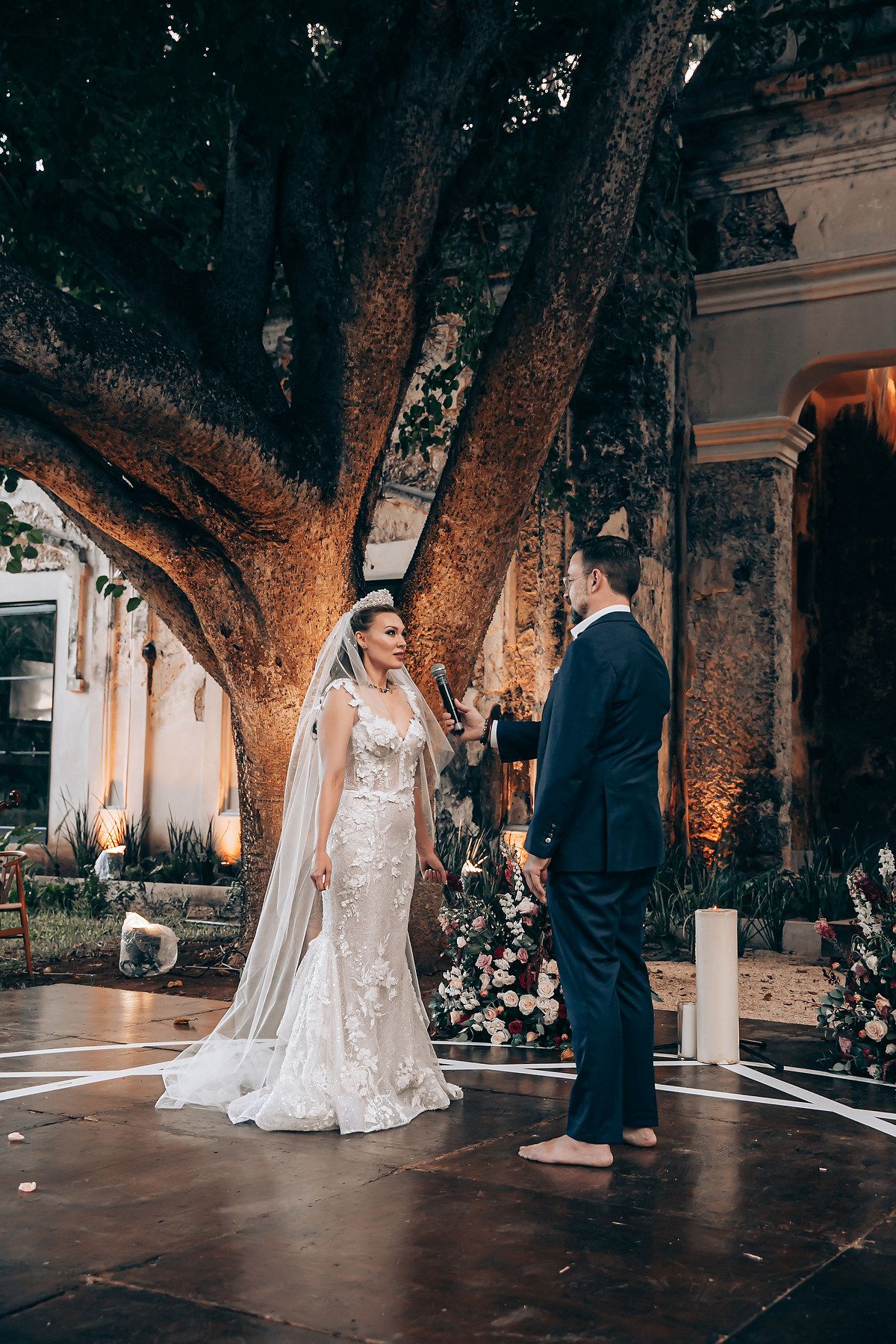 Elegant wedding ceremony taking place under illuminated trees at dusk.
