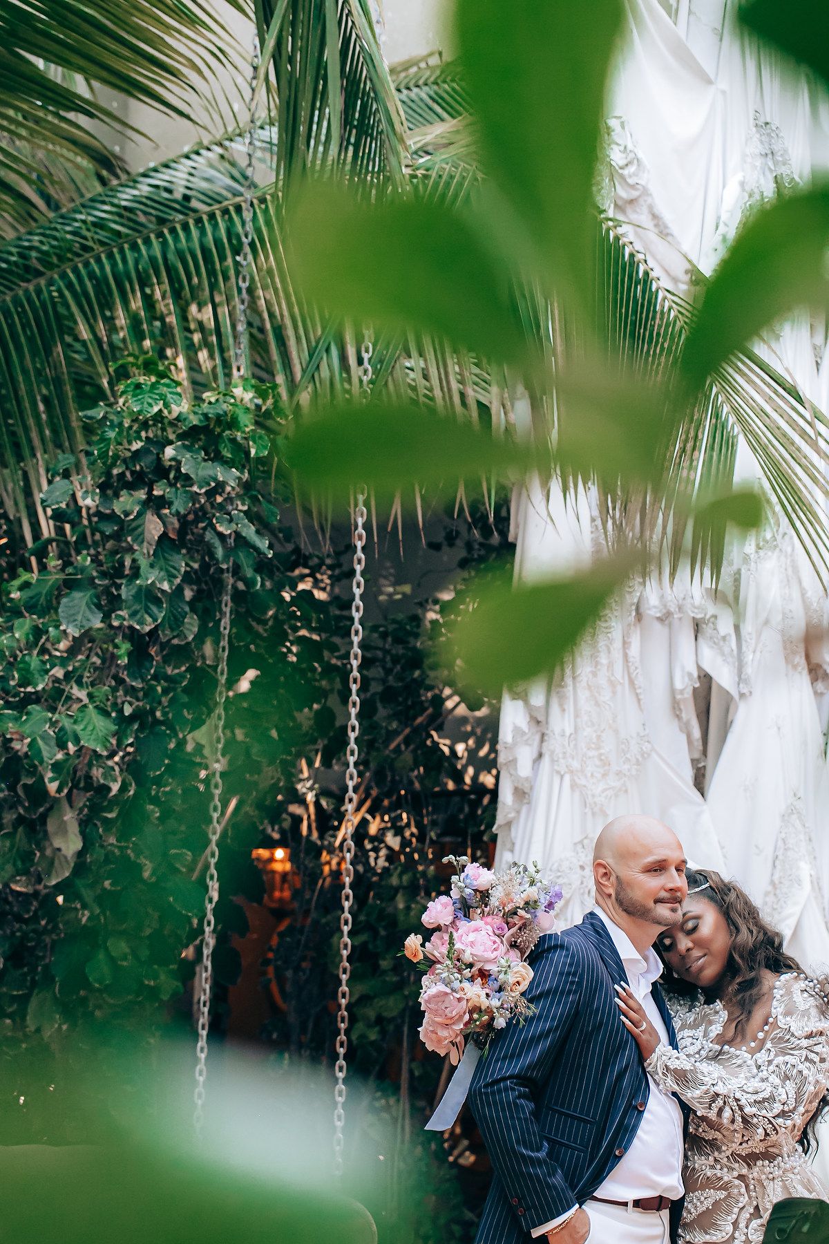 Romantic wedding portrait through tropical foliage with pink floral bouquet.