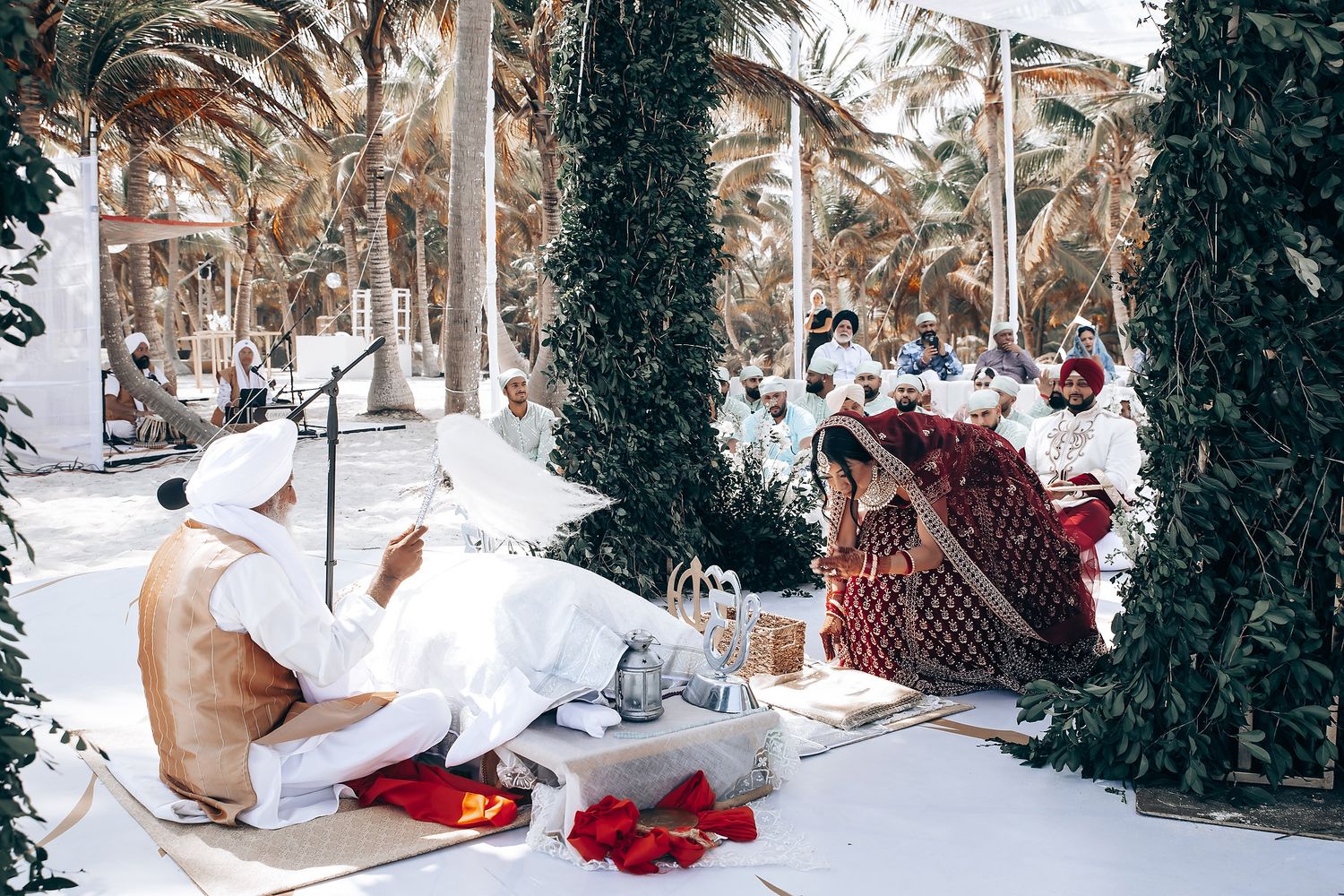 Wedding guests seated on white cushions during an outdoor ceremony.