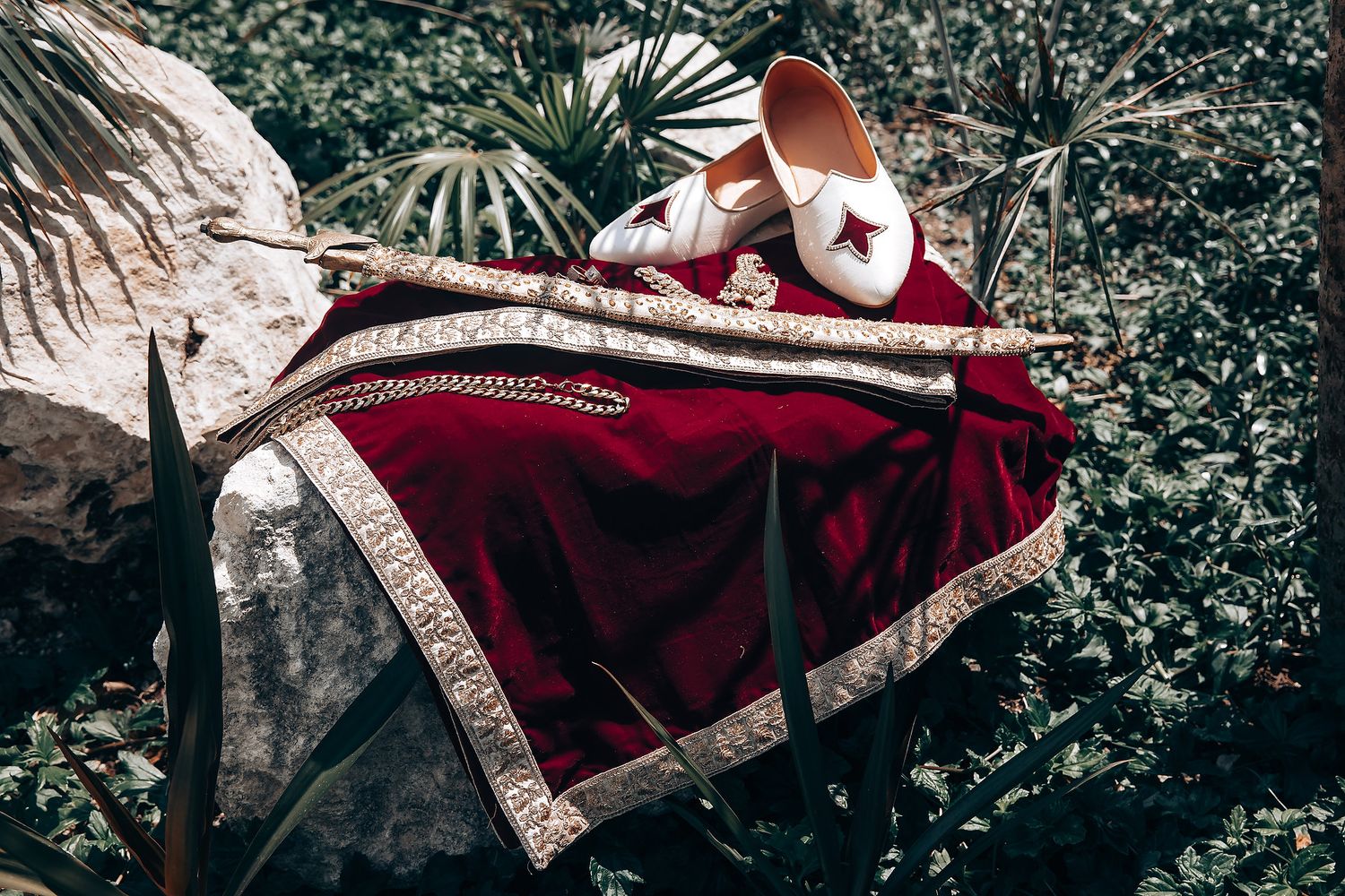 Rich burgundy and gold wedding attire details against a natural backdrop.