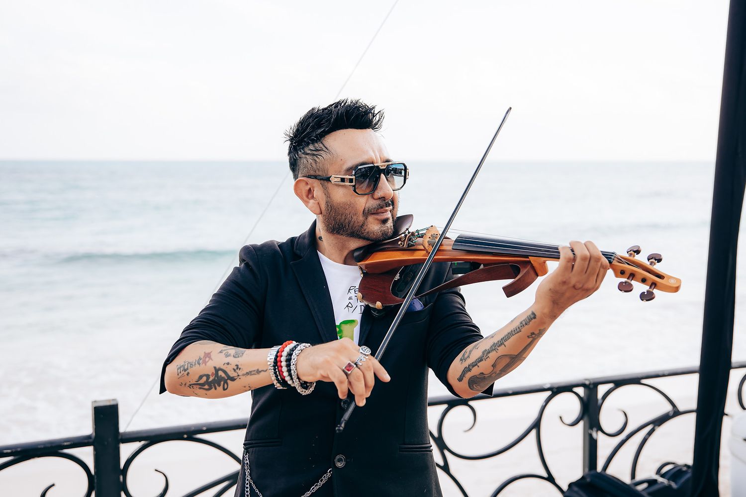 Two musicians perform on violins while seated outdoors against an ocean backdrop.