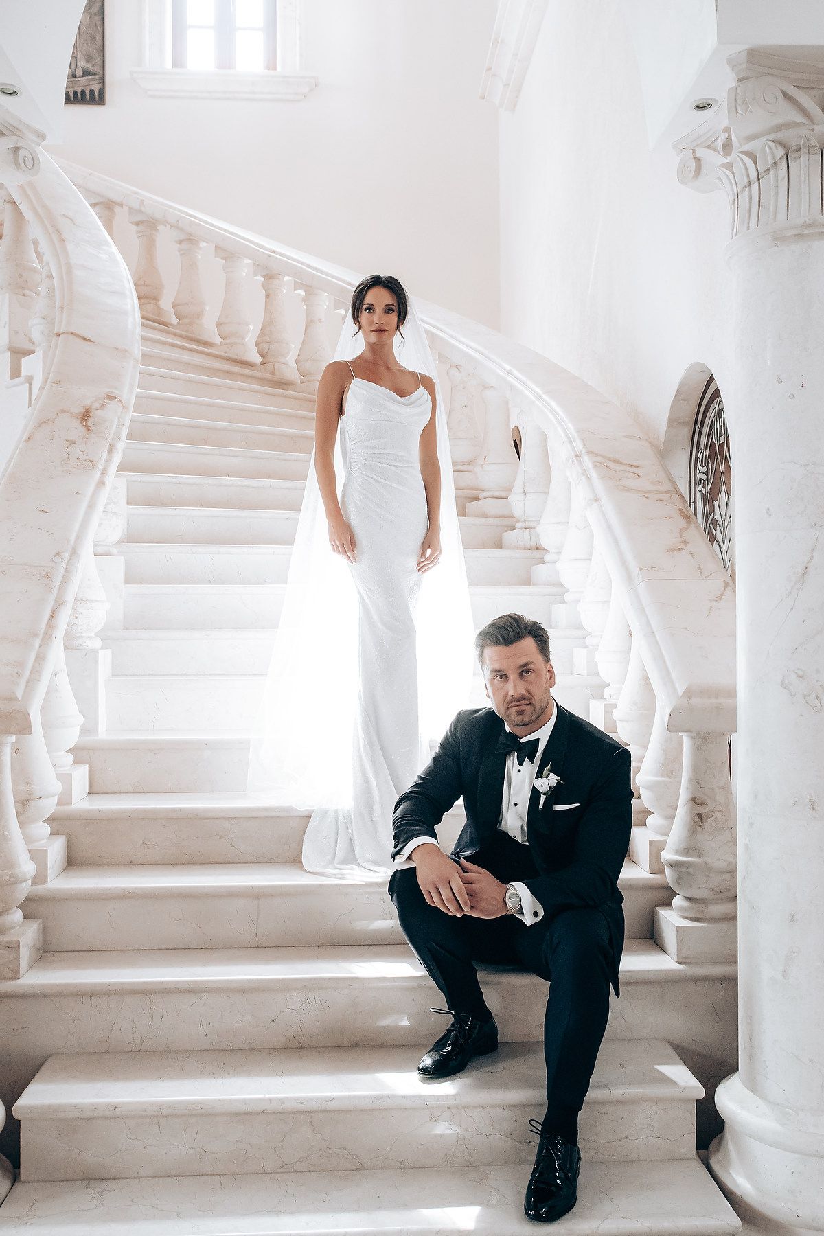A black and white wedding photo series showing a couple posing on elegant white marble stairs.