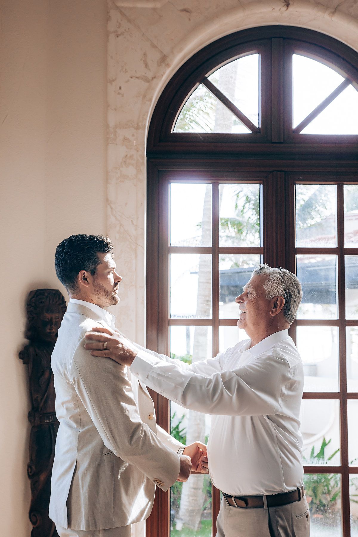 Two people in white shirts practice martial arts moves together in a bright interior space with arched windows.