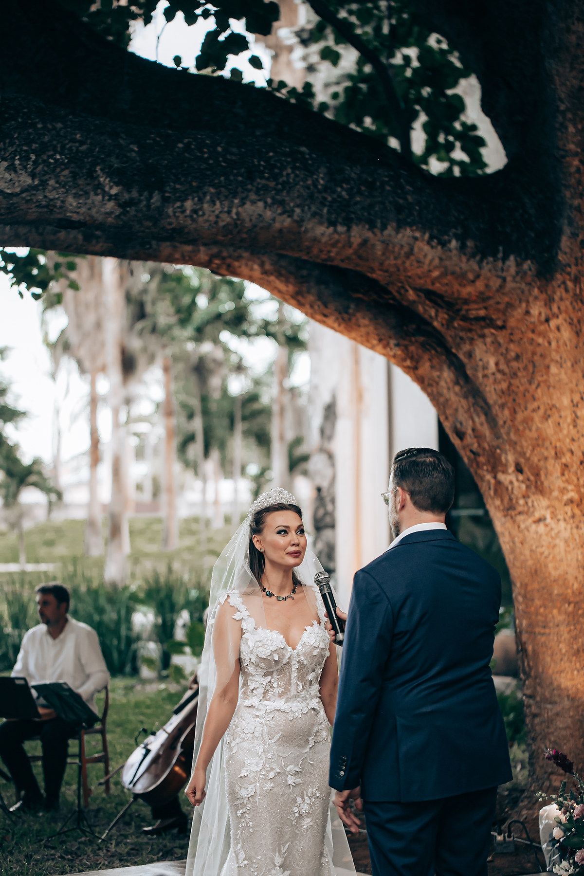 A romantic wedding scene under a large tree with the couple sharing intimate moments in a beautiful outdoor setting.