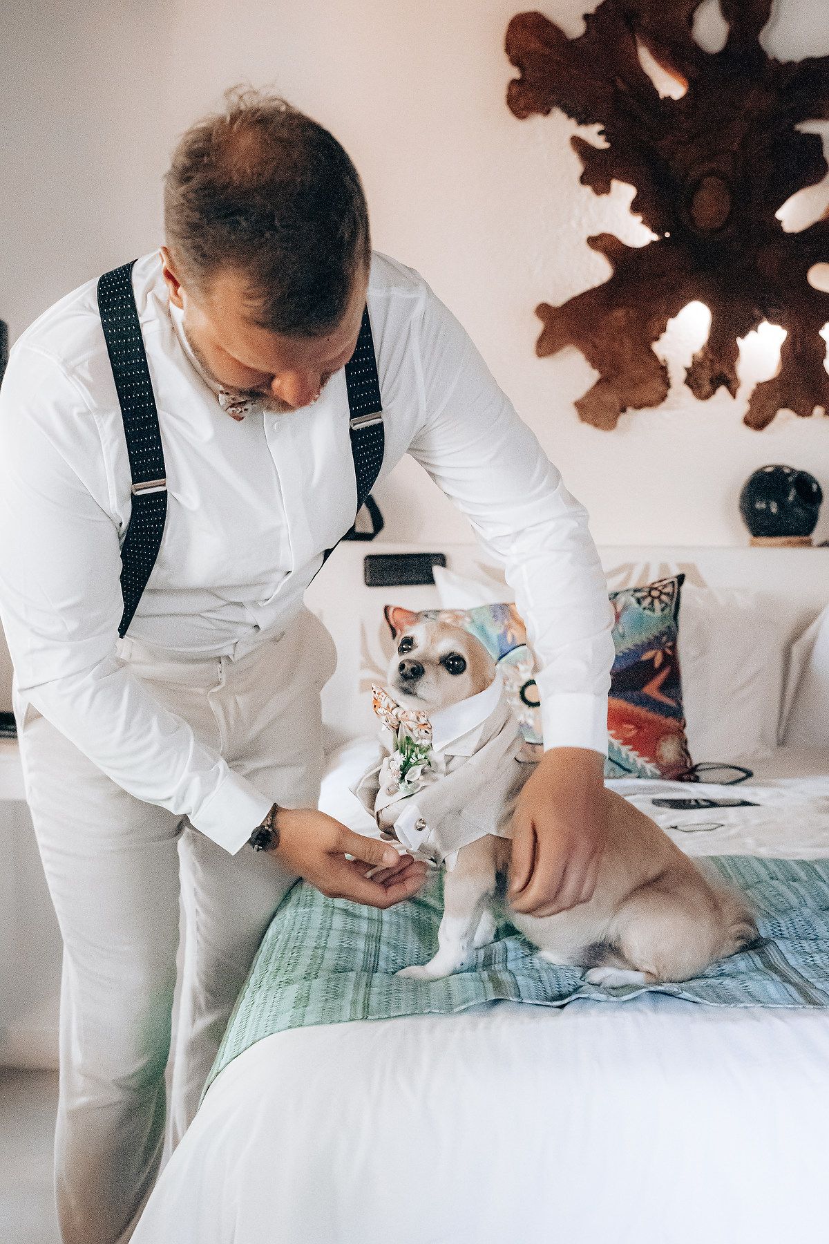 A person wearing white attire and suspenders carefully attends to a small pet lying on a mint green blanket.