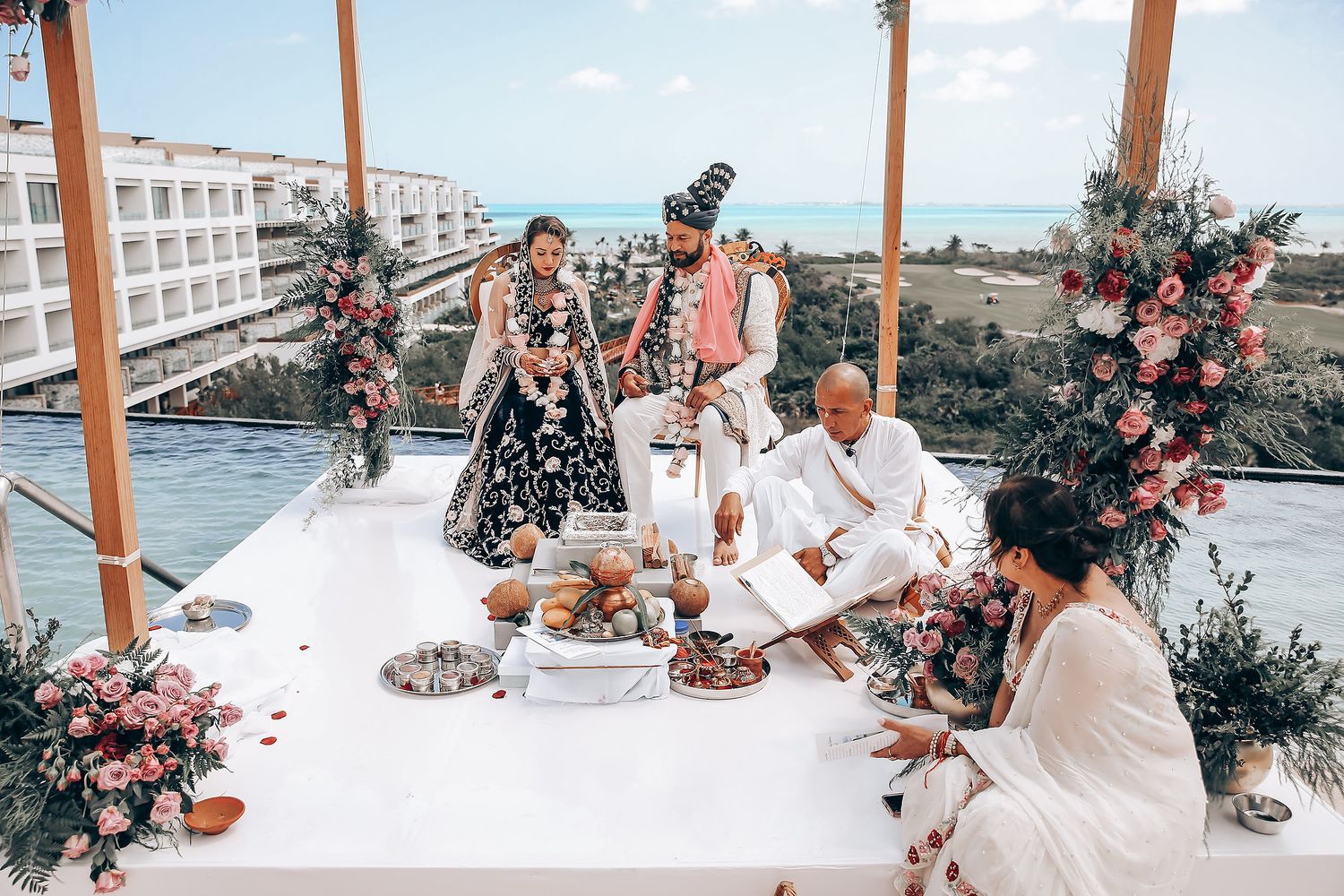 A romantic beachside wedding ceremony setup with white decor, wooden posts, and floral arrangements.