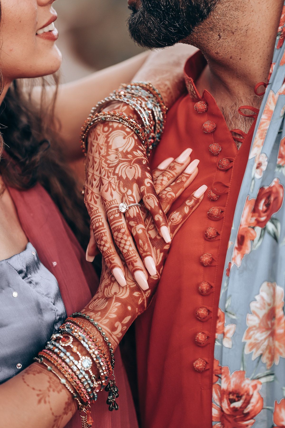 Close-up of intricate henna design on hands with silver bangles against red traditional Indian wedding attire.