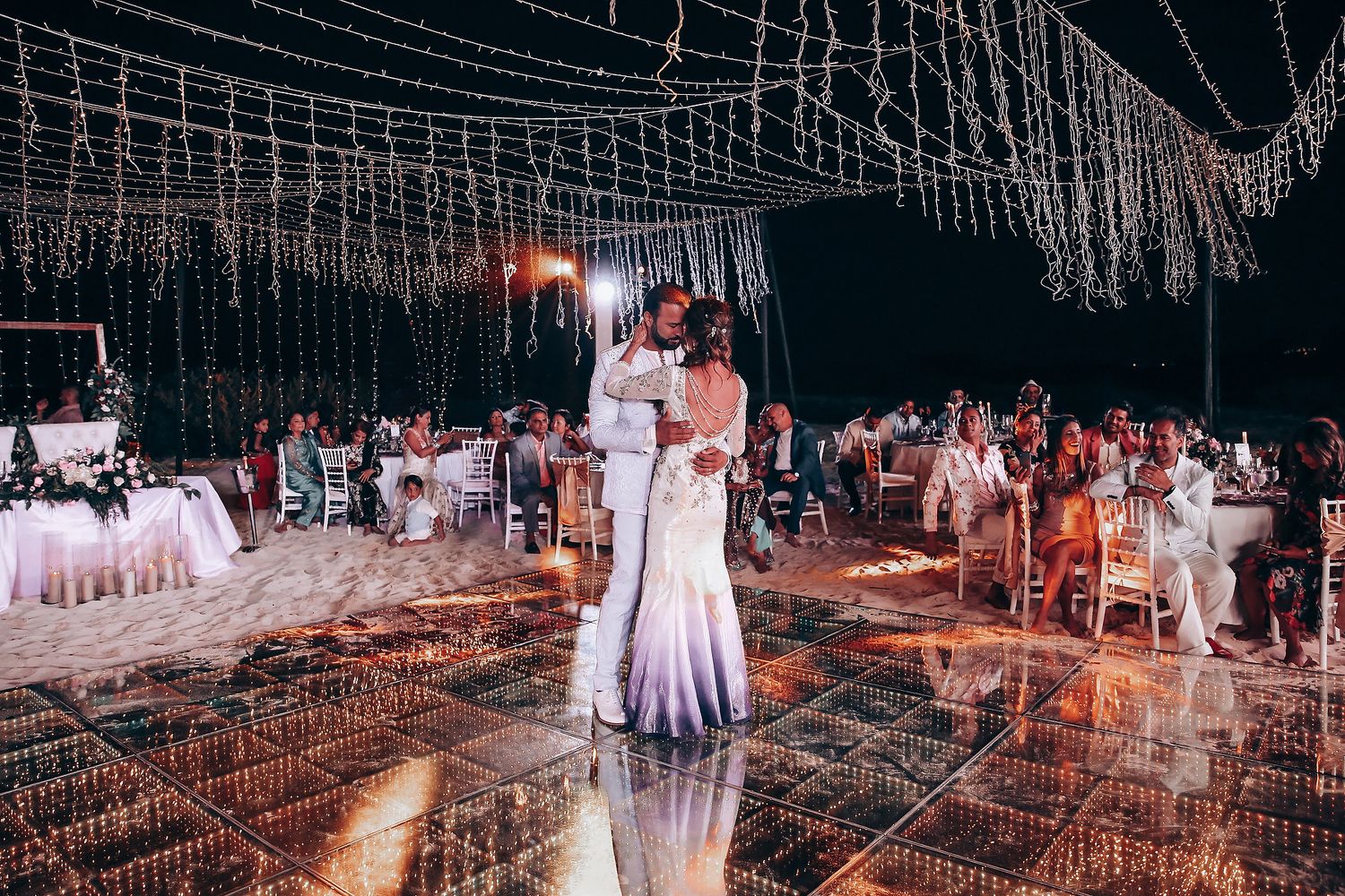 Elegant outdoor wedding reception setup with string lights and white decor creating a romantic ambiance at night.