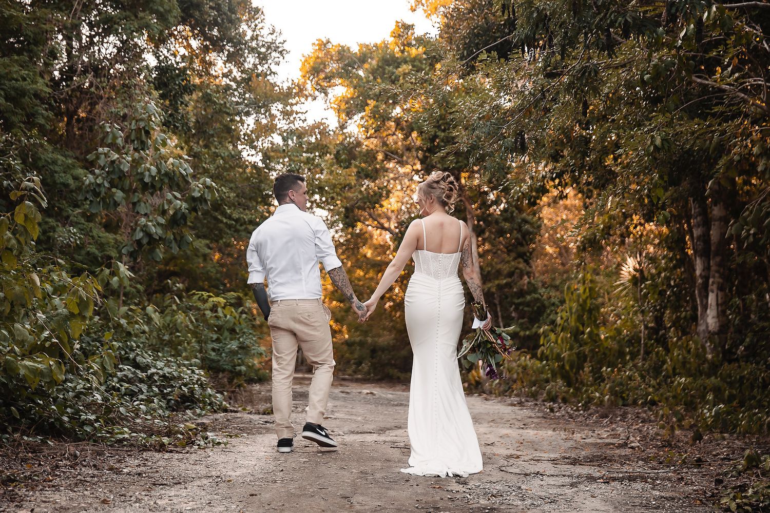 A couple walks hand in hand down a tree-lined path during golden hour.