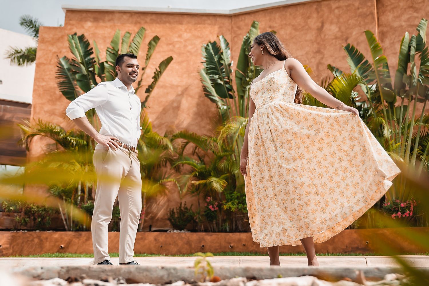 Couple dancing together near a terracotta wall surrounded by tropical plants.