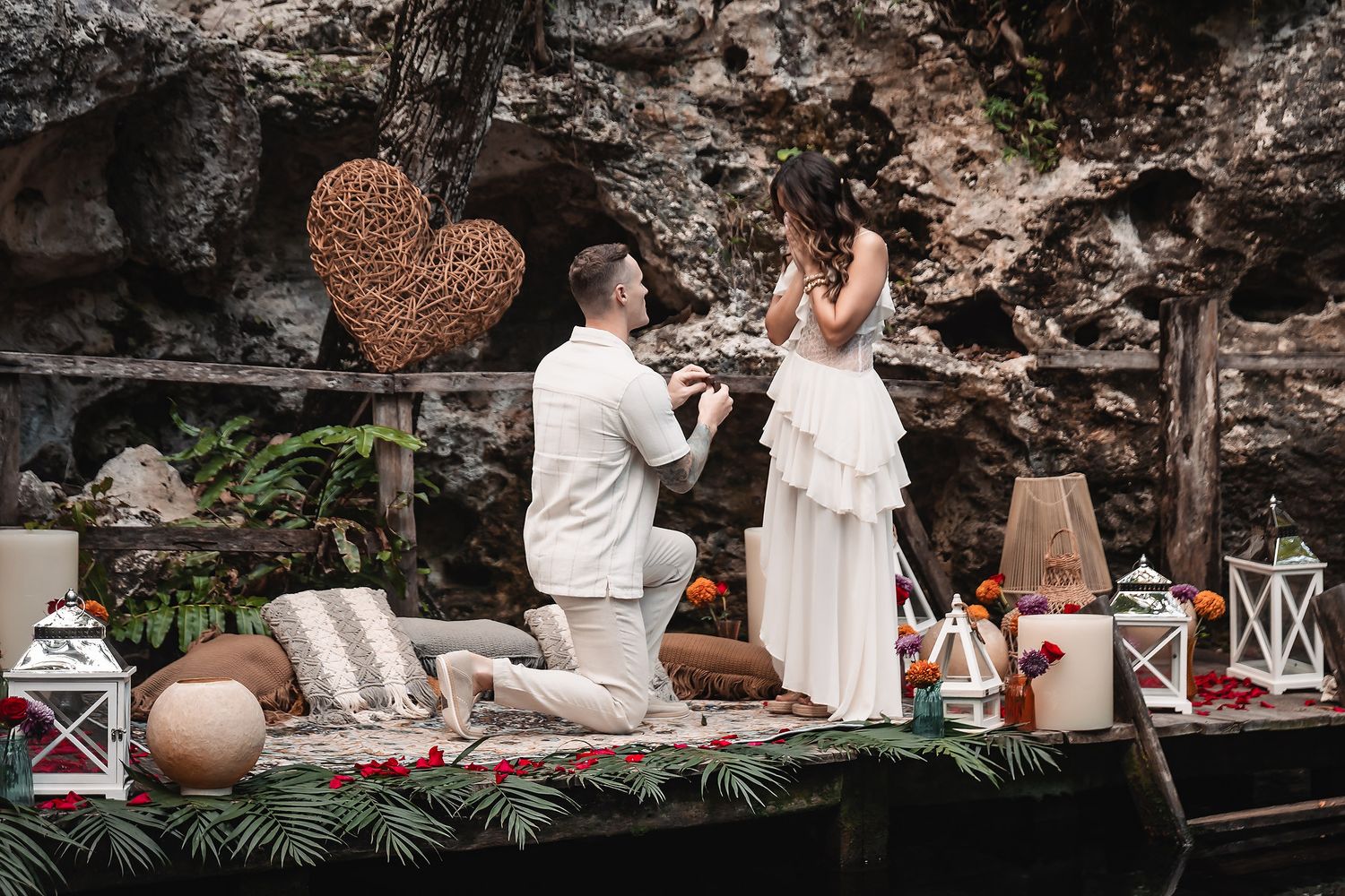 Marriage proposal scene on a decorated platform with lanterns and rose petals against rocky backdrop.