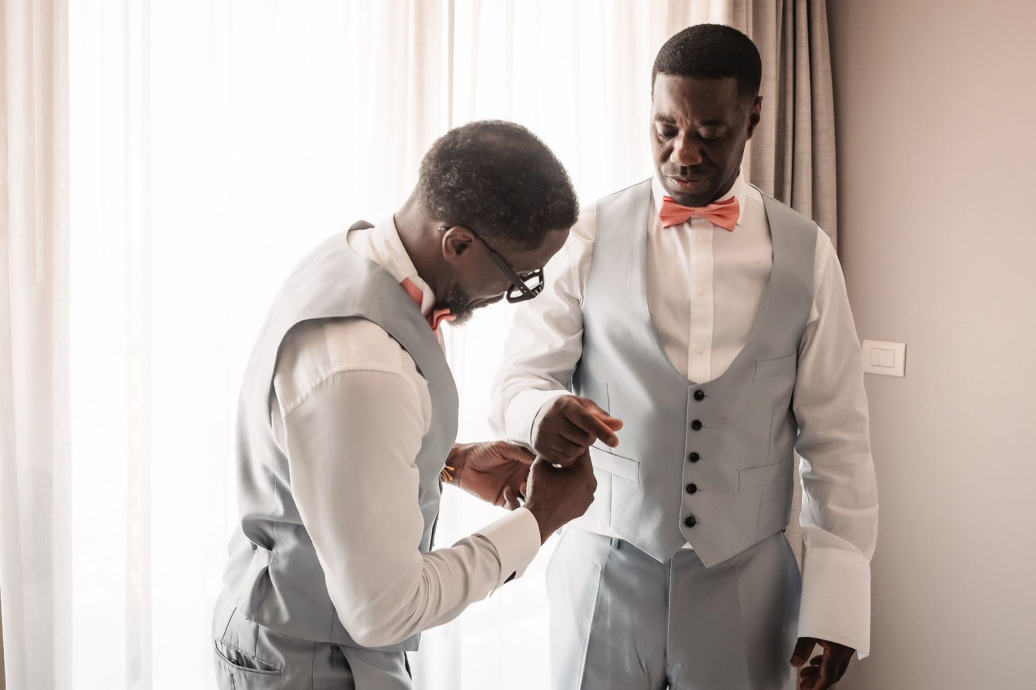 Groomsmen in light gray vests and bow ties prepare for a wedding ceremony.