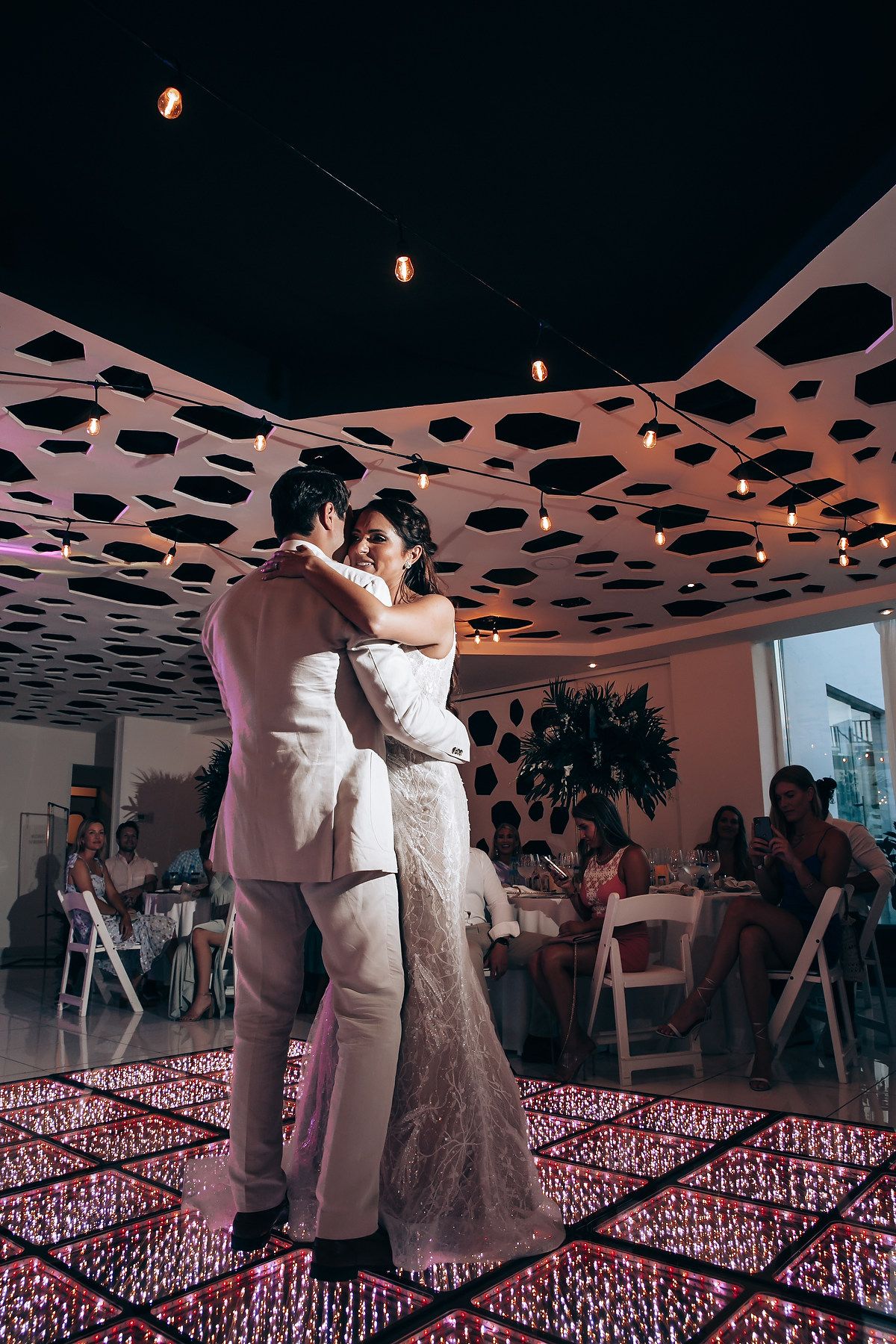 First dance at wedding reception under unique perforated ceiling with warm lighting.