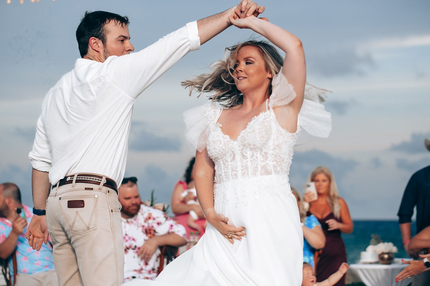 Couple dancing at a beach wedding celebration with guests watching in the background.