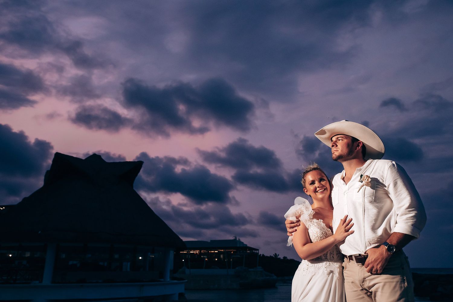 Dramatic sunset sky with purple clouds over beach wedding celebration.