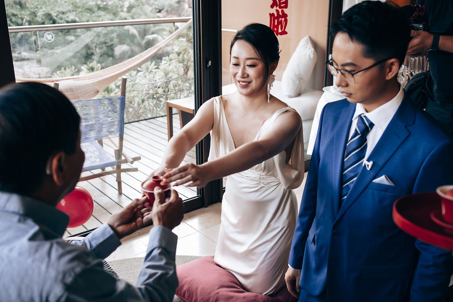 Wedding guests seated in a room with traditional Chinese decorations and natural lighting.