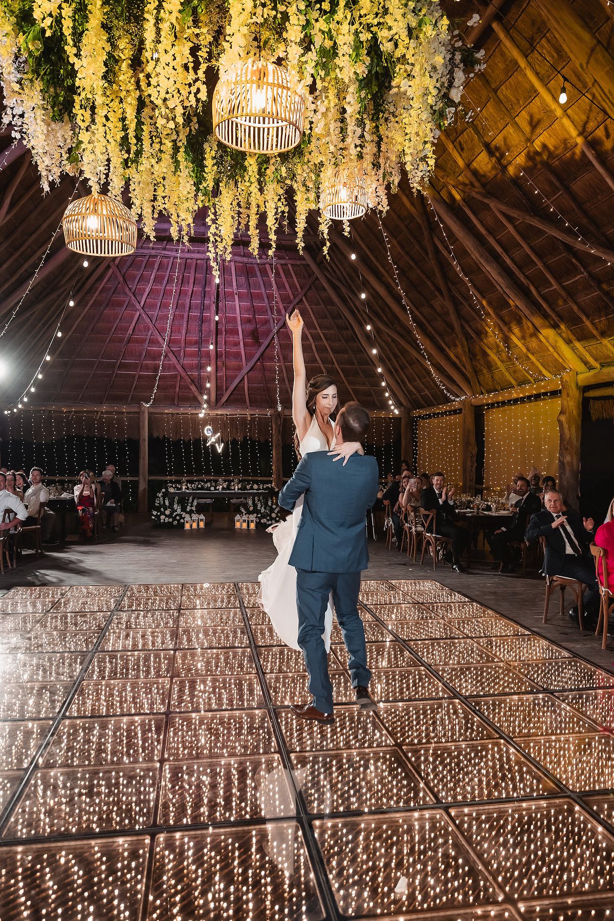 Rustic barn wedding venue with dramatic yellow floral chandeliers and rows of candles.